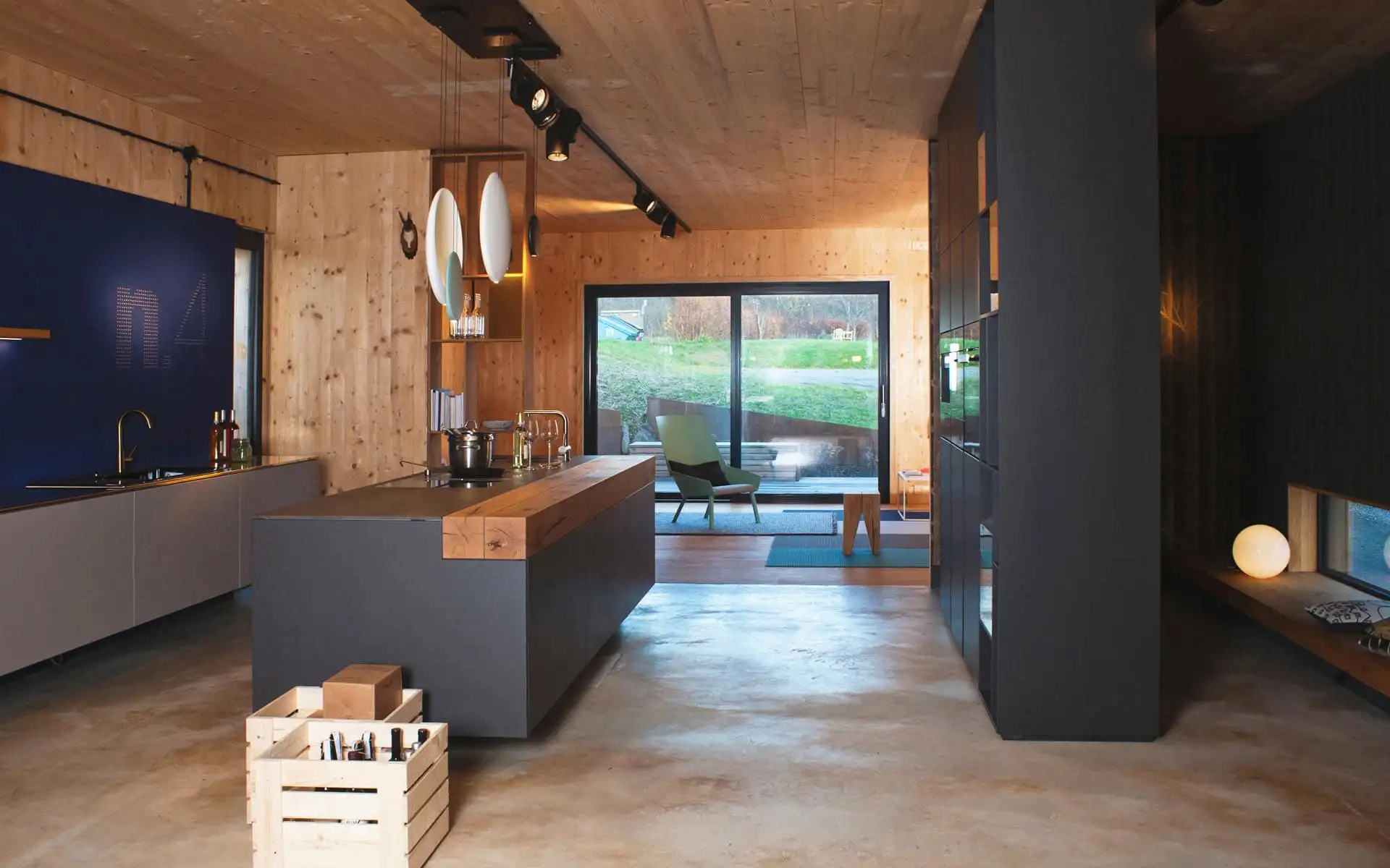 Offene Wohnküche mit zentraler Kochinsel, Holzdecke, integrierter Beleuchtung und Blick in den angrenzenden Wohnbereich.