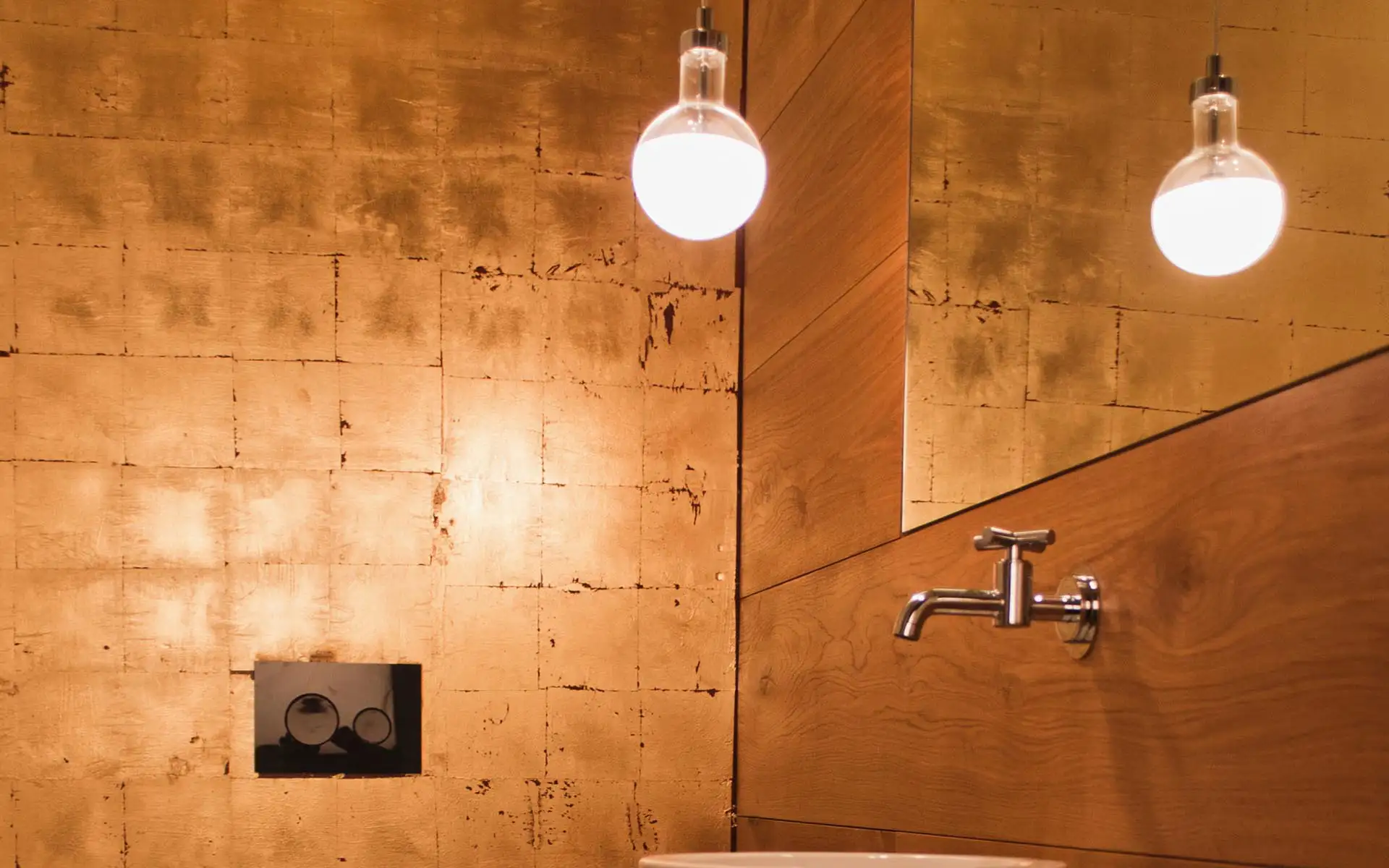 Sanitärbereich mit wandbündigem Waschtisch, Armatur und warm beleuchteter Wandoberfläche.