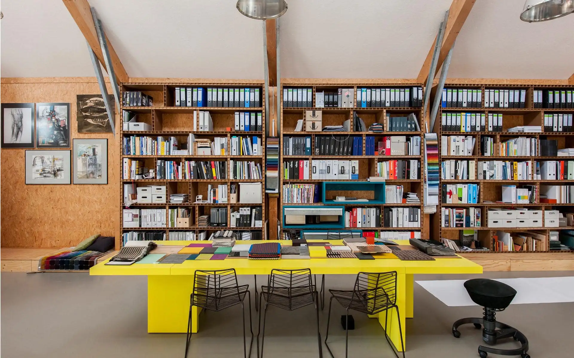 Innenraum mit langem Arbeitstisch, Materialauswahl, Regalsystem und Sitzgelegenheiten.