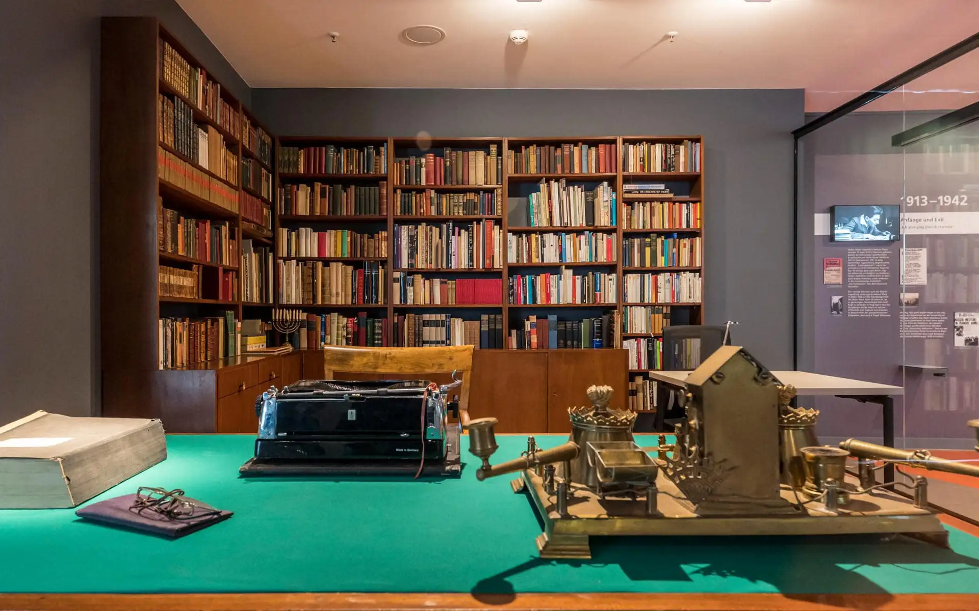 Rekonstruiertes Arbeitszimmer von Stefan Heym hinter Glas: grüner Schreibtisch mit Schreibmaschine, davor Objekte, dahinter eine Raum hohe Bücherwand