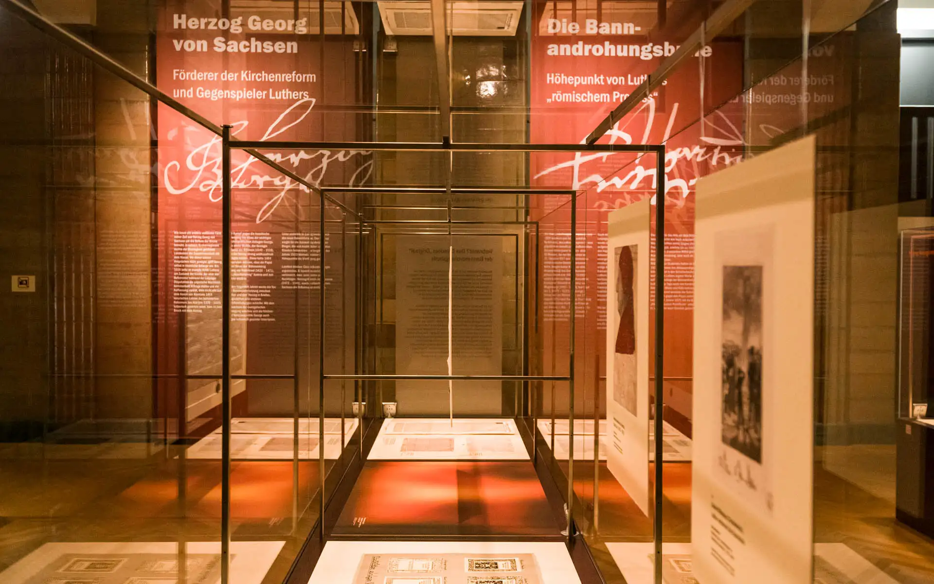 Vitrinen-Gang mit historischen Dokumenten, rote Wandtexte zu Herzog Georg von Sachsen und Luthers Bannandrohungsbulle