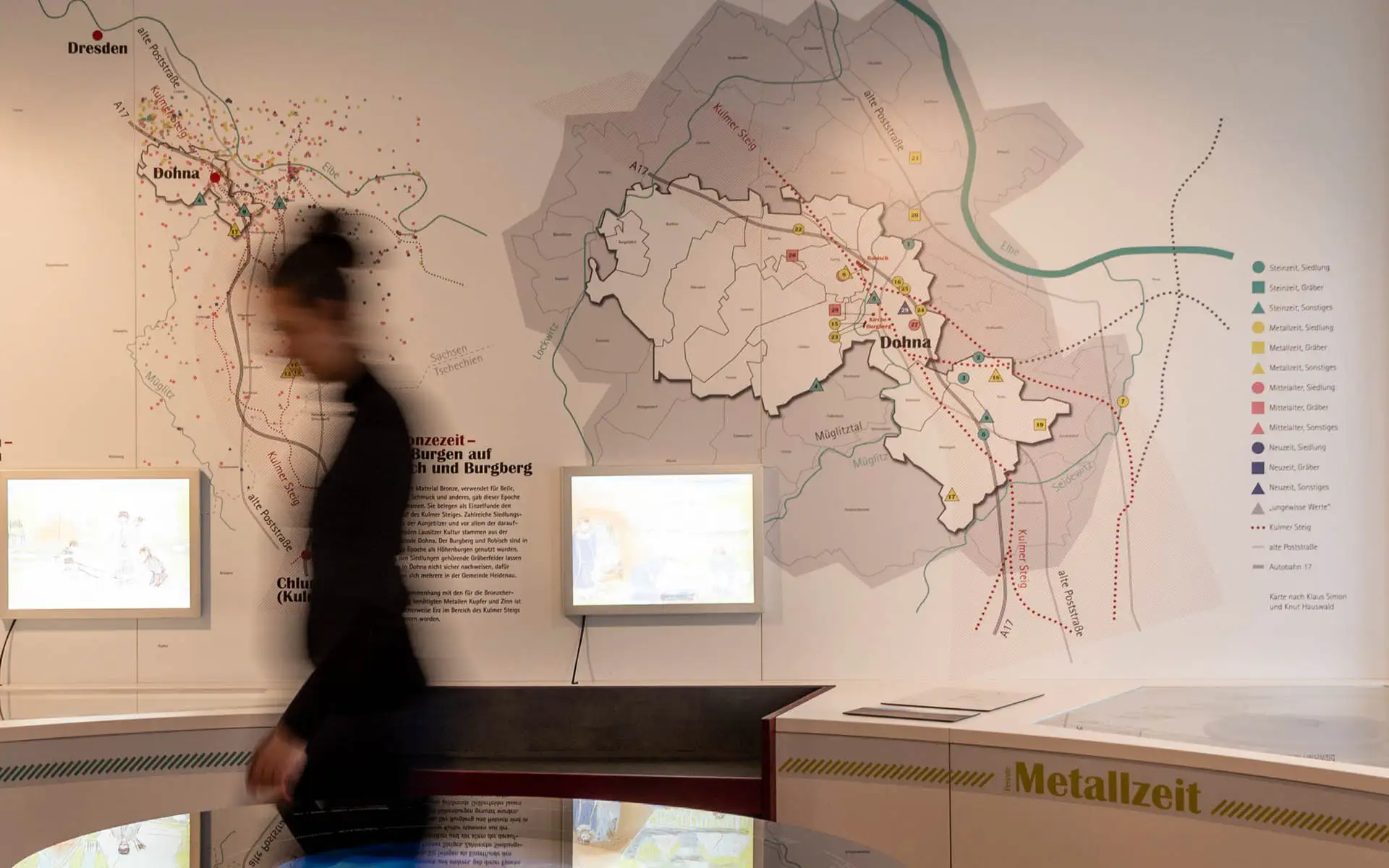 Wandgrafik mit großformatiger Karte von Dohna und dem Kulmer Steig; Infografik mit Legende, davor eine Besucherin in Bewegung.