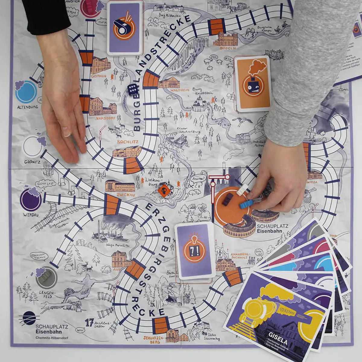 Ausgelegter Spielplan mit Karten, Spielfiguren und Händen beim Spielaufbau