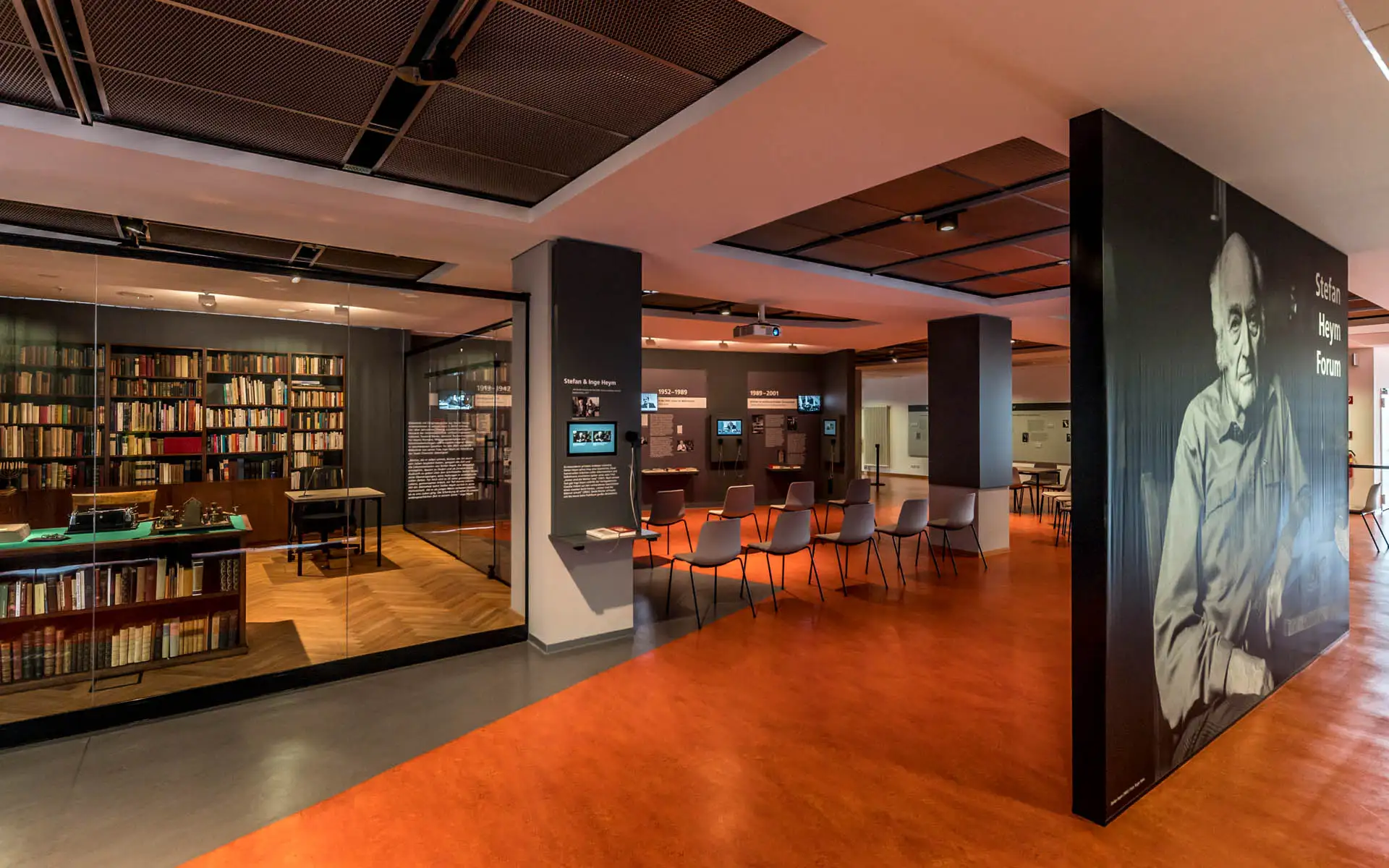 Blick in das Stefan-Heym-Forum: Bibliothek hinter Glas links, Stuhlkreis und Medienstationen im Ausstellungsraum, rechts großformatiges Porträt