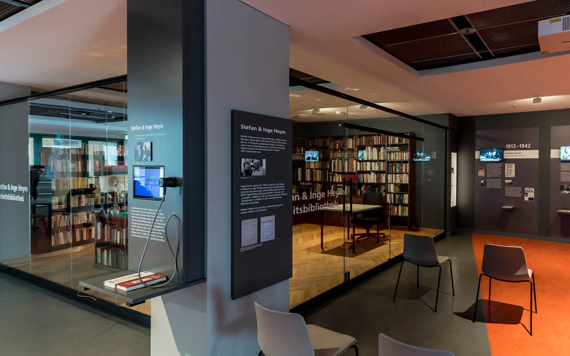 Infostele ‚Stefan & Inge Heym‘ mit Bildschirm und Kopfhörer im Vordergrund, dahinter die verglaste Arbeitsbibliothek