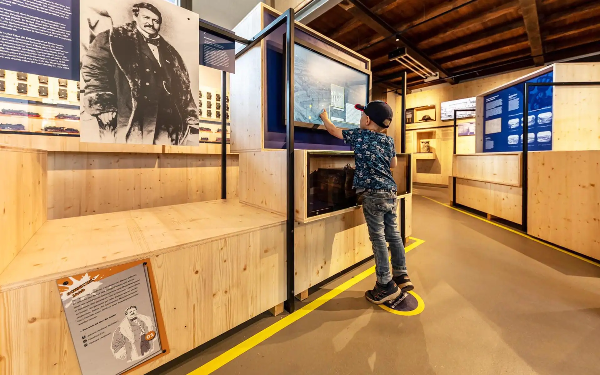Zwei schwarze Dampflokomotiven in der Halle, Besucher laufen vorbei