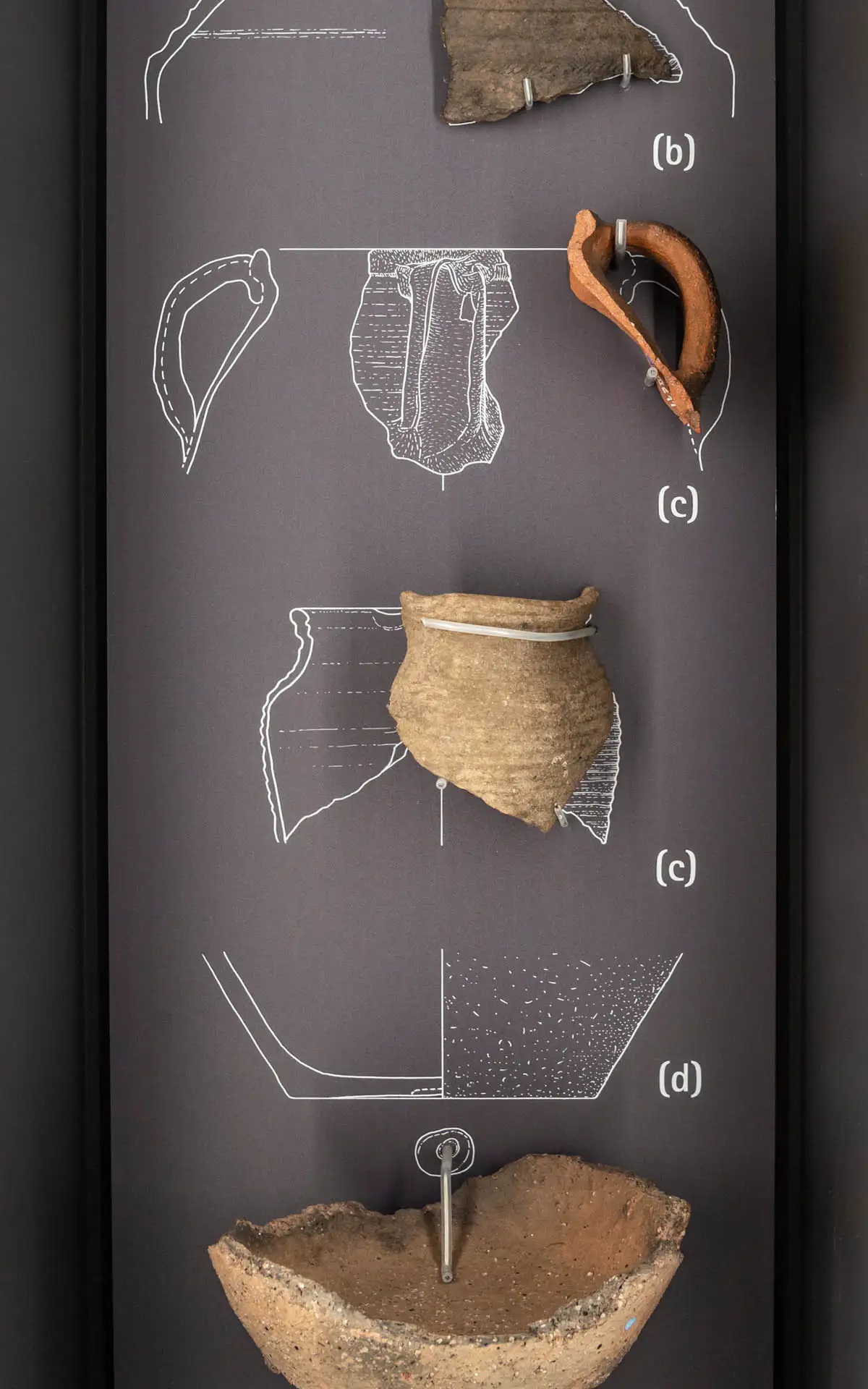 Keramikfunde auf dunkler Ausstellungstafel: Scherben und rekonstruierte Gefäßformen im Hochformat.