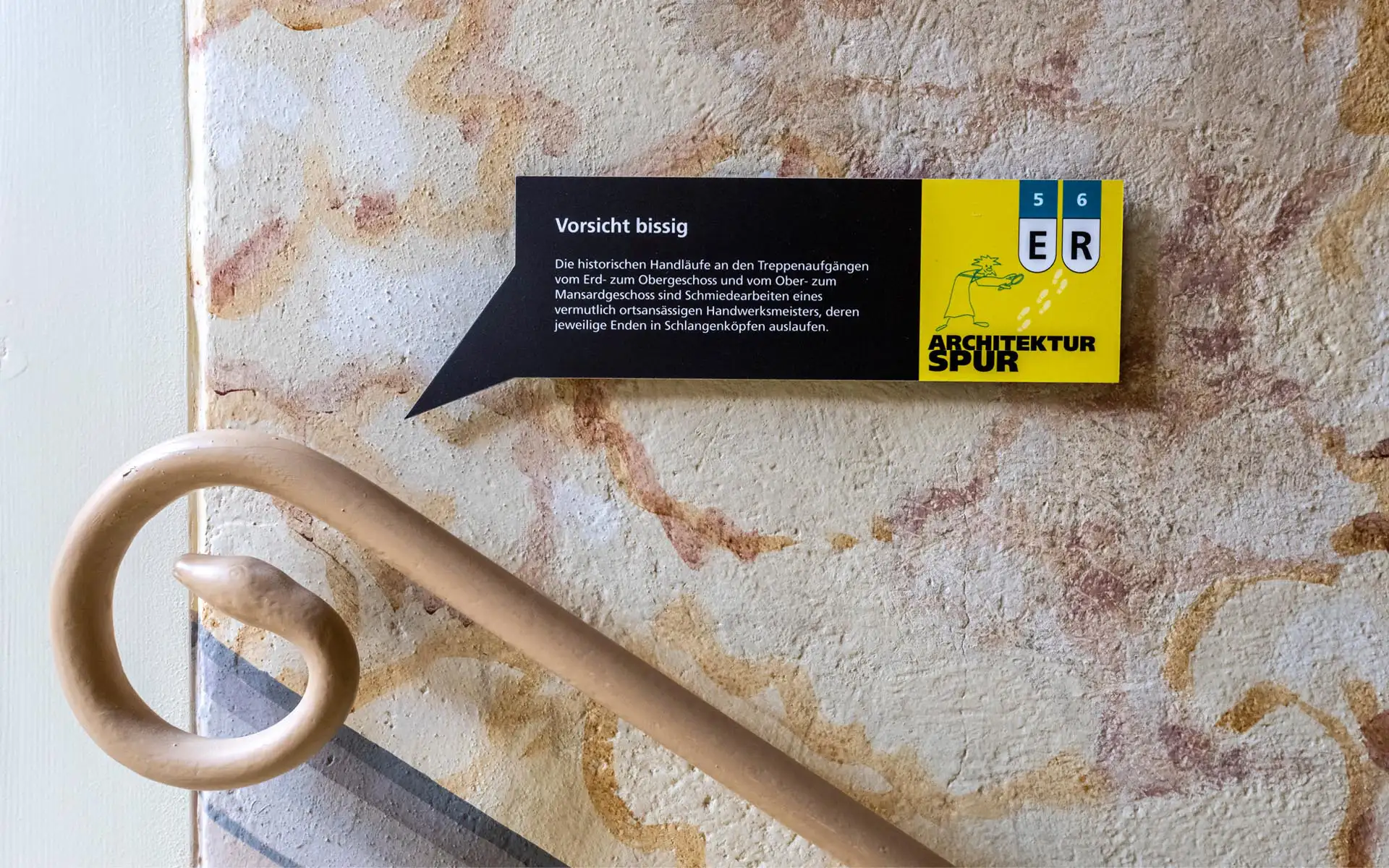 Hinweisschild 'Vorsicht bissig' an historischer Wand, Handlauf endet in Schlangenkopf