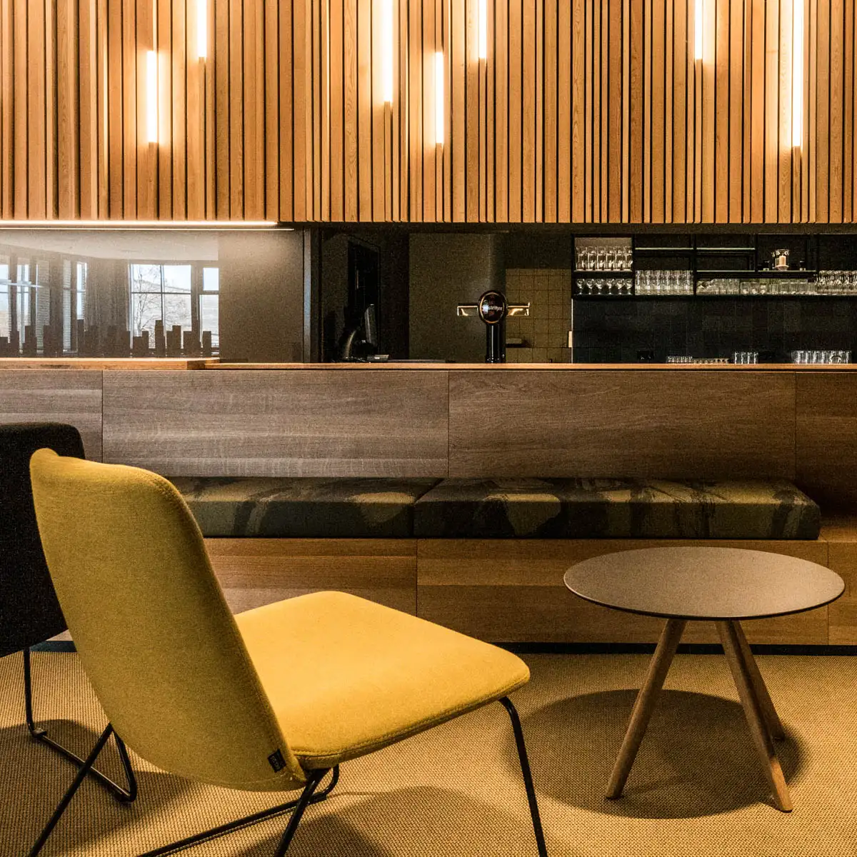 Nahaufnahme eines gemütlichen Loungebereichs mit gelben Sesseln vor einer Holzverkleidung.