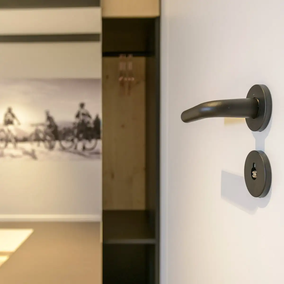 Detailansicht eines schwarzen Türgriffs vor dem offenen Schrank und Wandbild im Hotelzimmer.