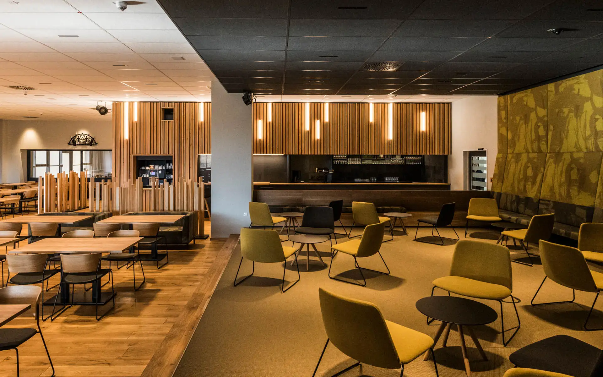 Großer Restaurantbereich mit gelben Loungesesseln, runden Tischen und beleuchteten Holzpaneelen.