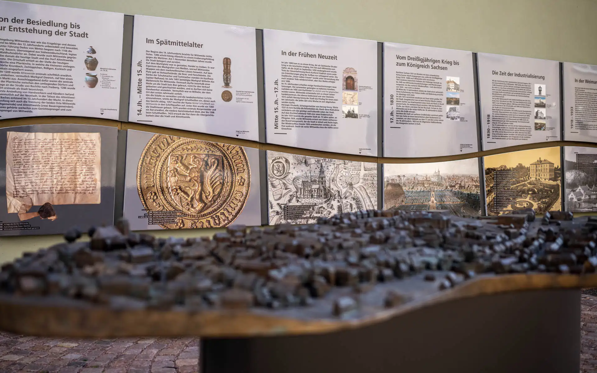 Wand mit historischen Tafeln und Stadtansichten; im Vordergrund das Bronze-Stadtmodell von Mittweida