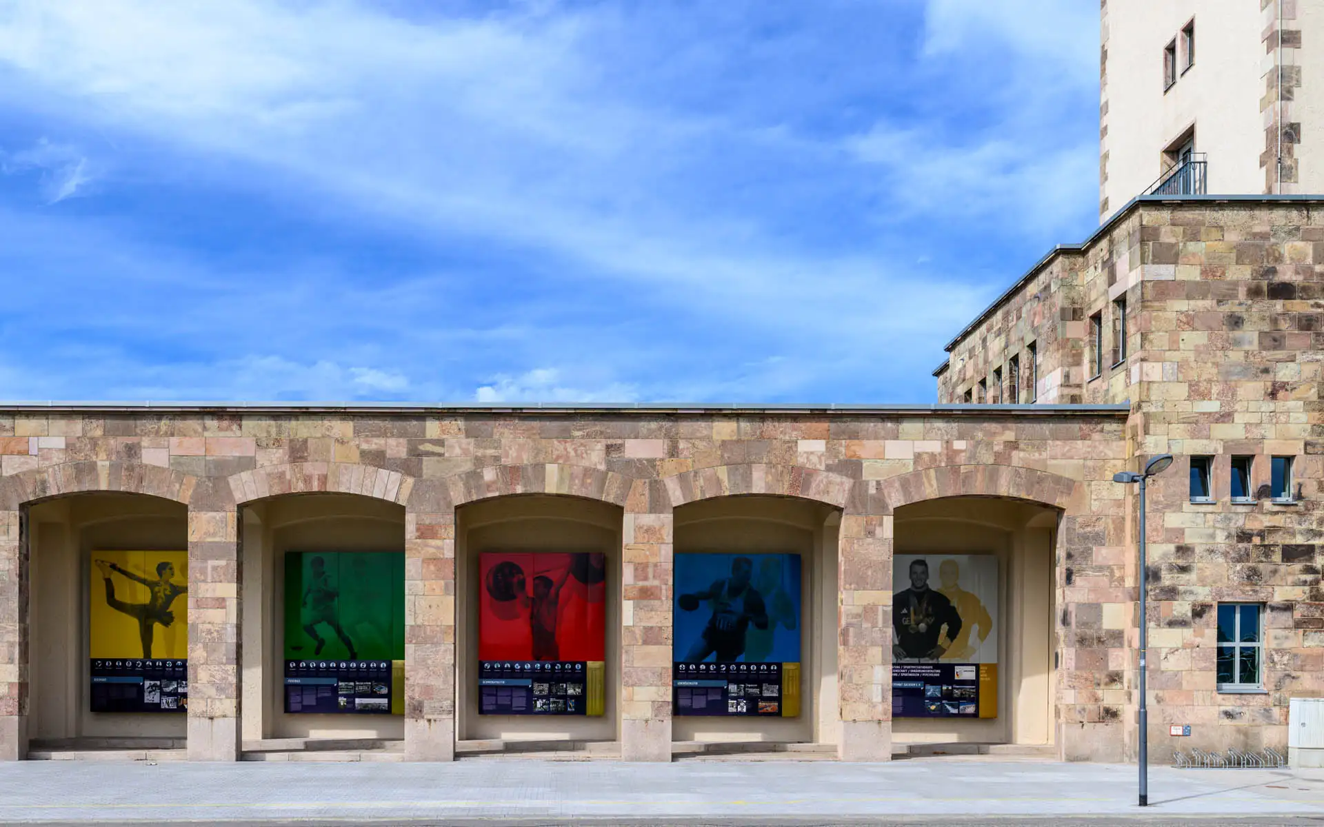 Portikus mit fünf farbigen Sportmotiven in den Nischen – Gelb, Grün, Rot, Blau und Weiß