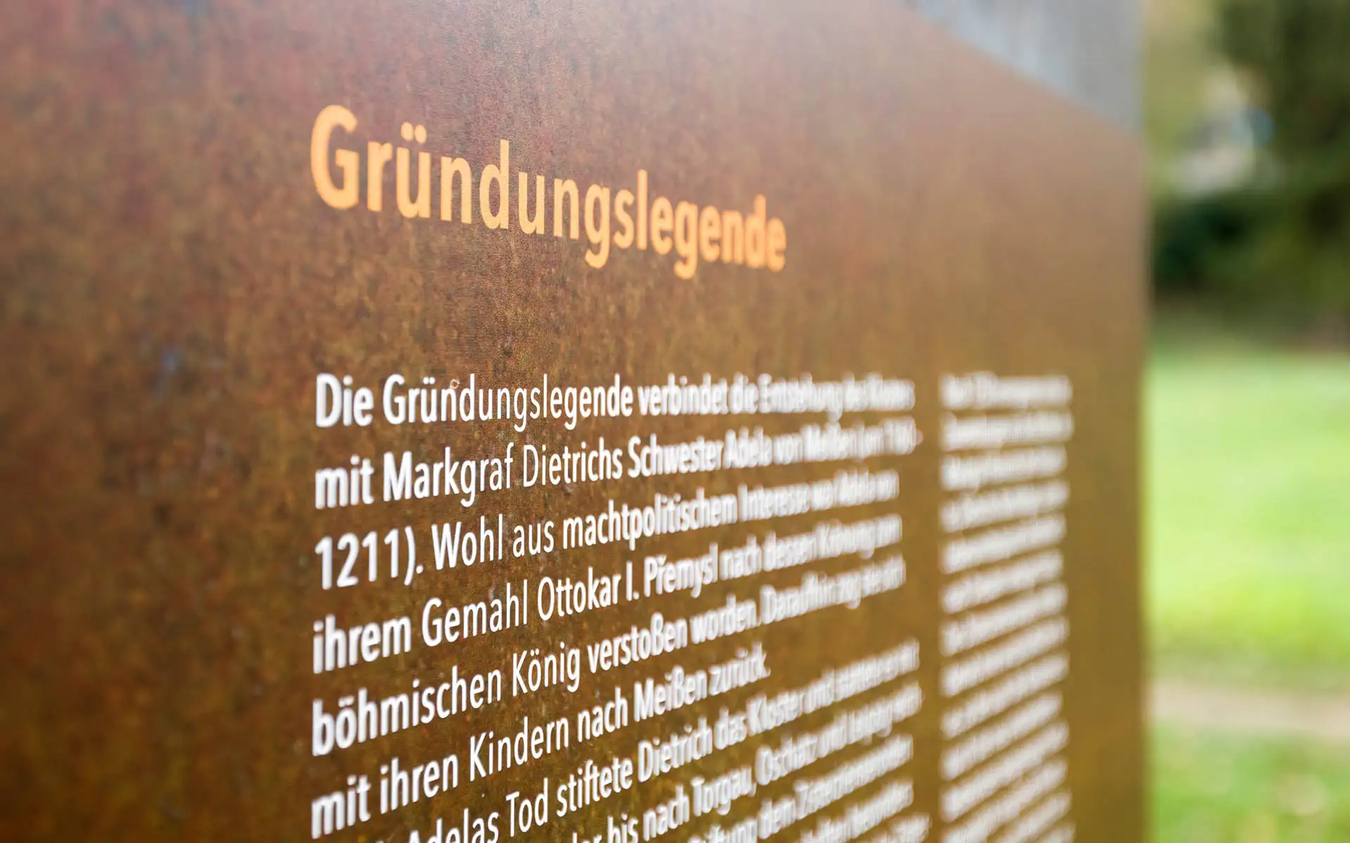 Nahaufnahme der Tafel Gründungslegende mit Text auf rostfarbener Metalloberfläche