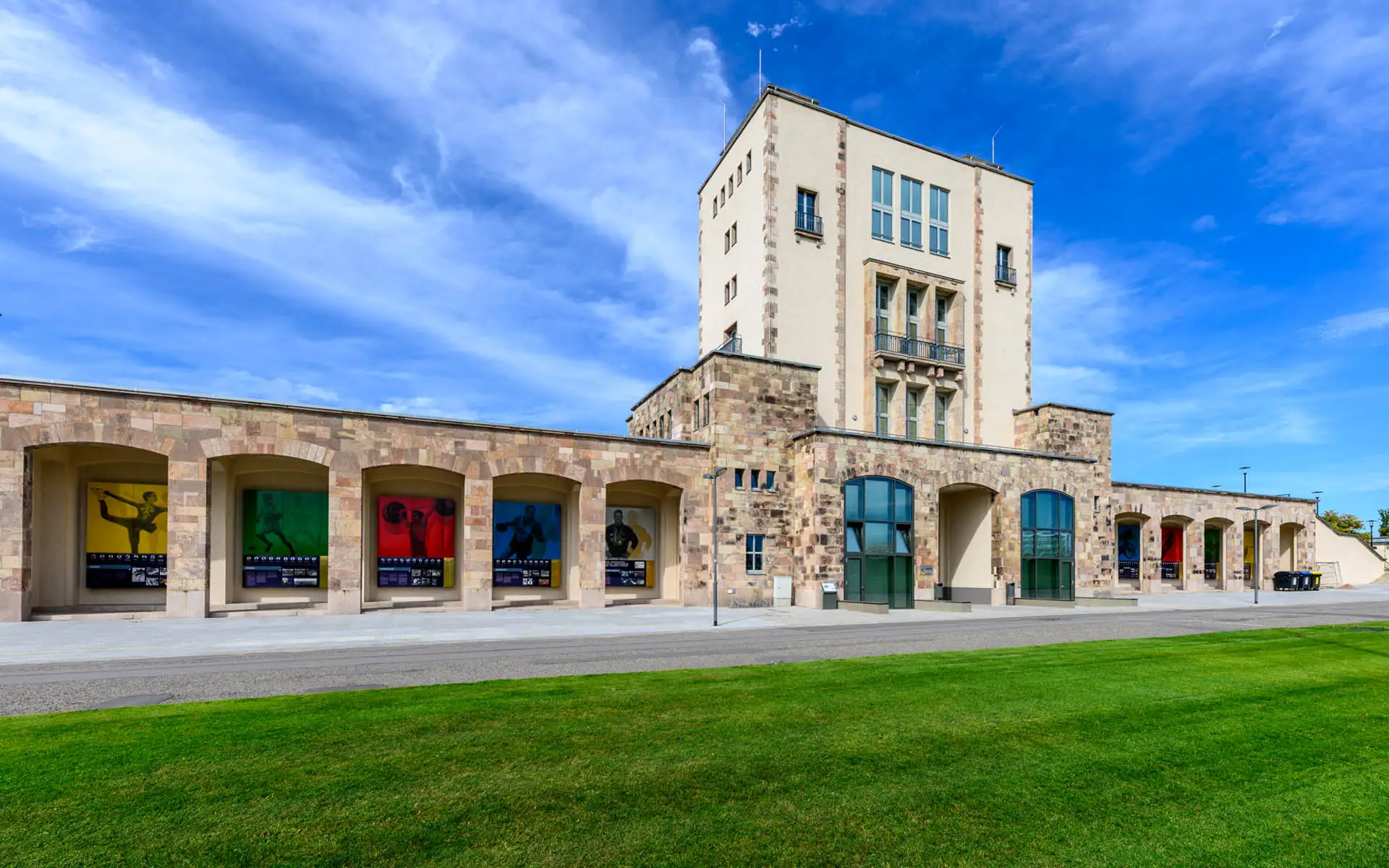 Außenansicht des Sportforums mit großformatigen farbigen Illustrationen in den Arkaden.