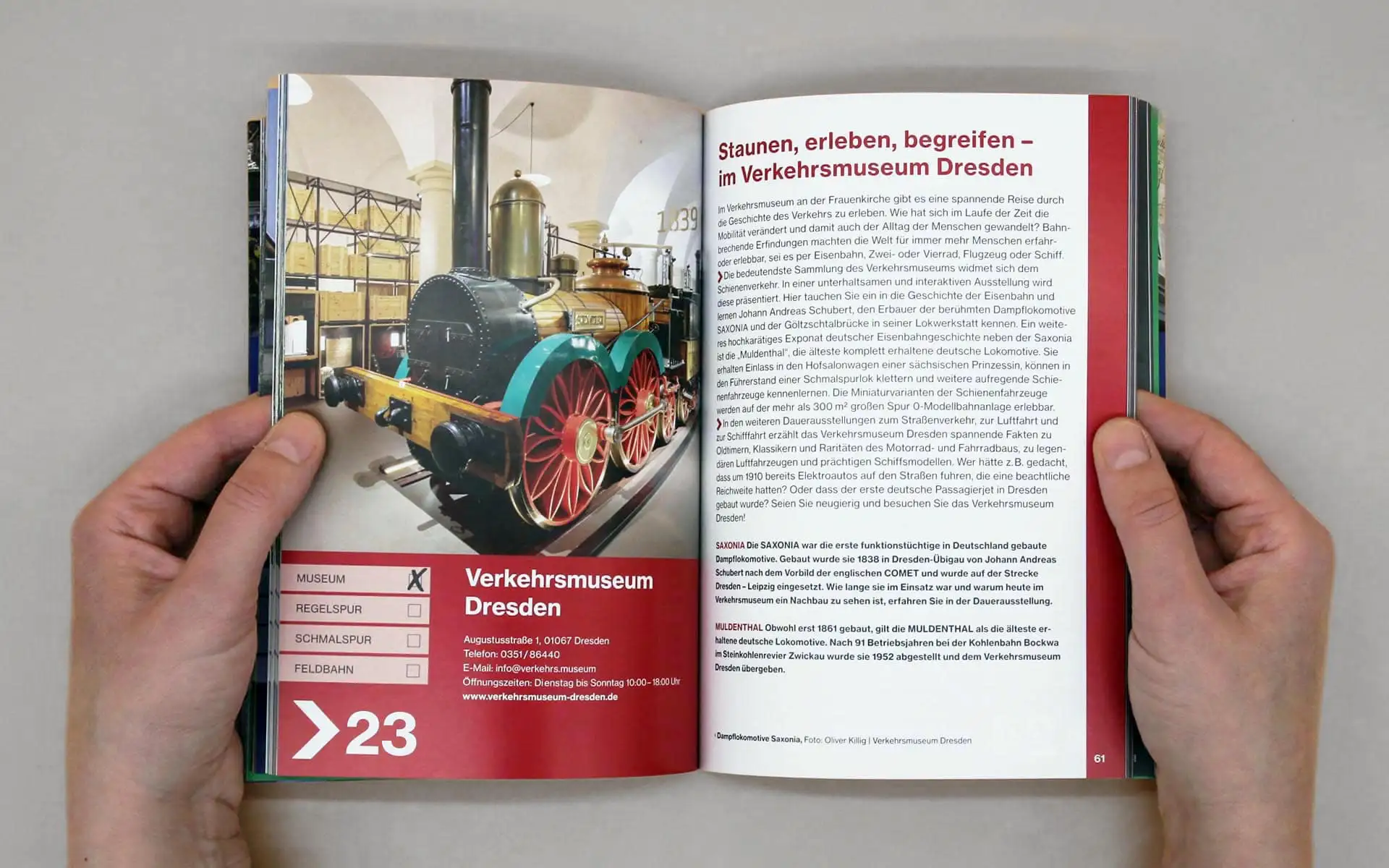 Aufgeschlagene Broschüre mit Foto einer historischen Lokomotive links und Textlayout mit roten Akzentflächen rechts.