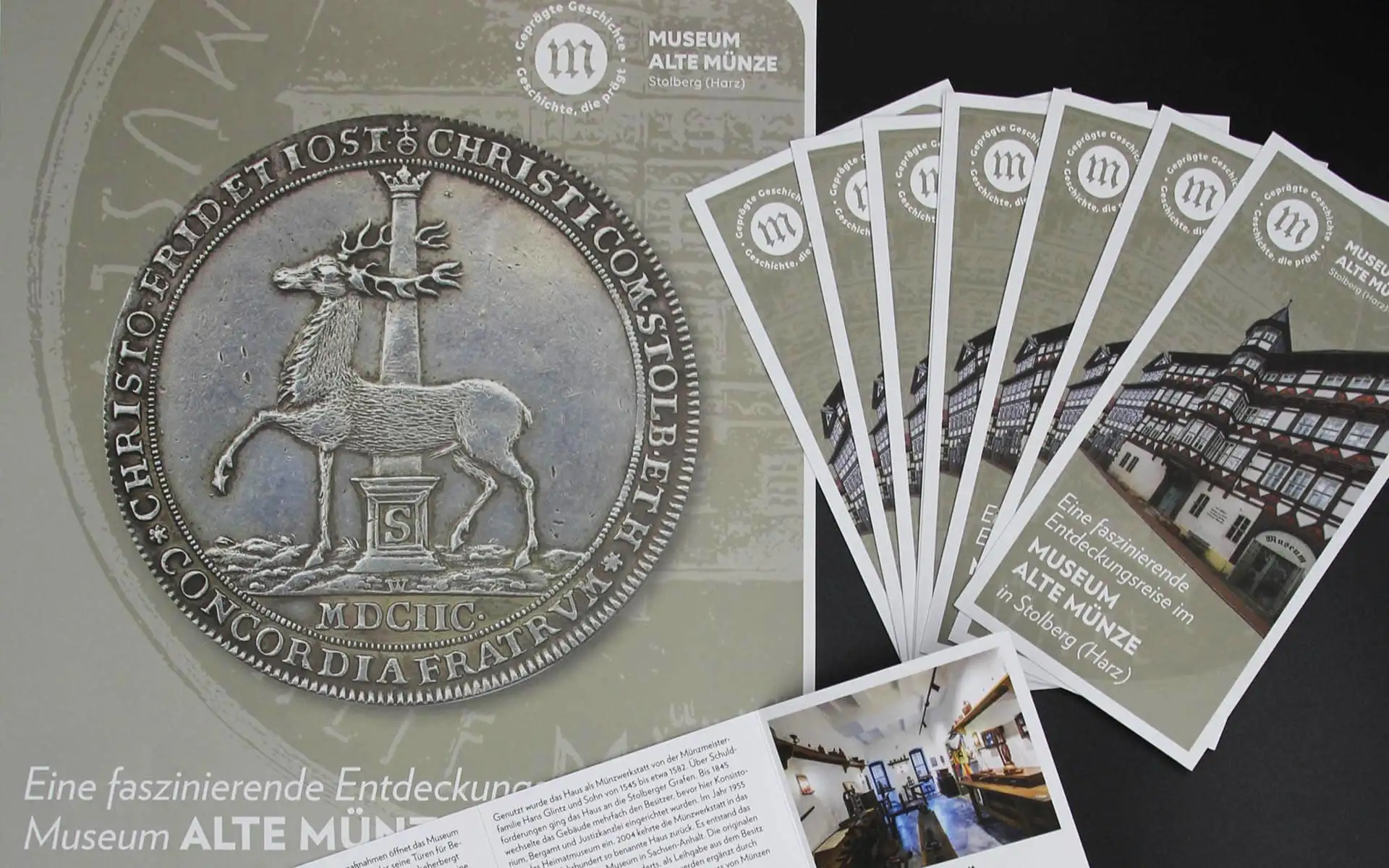 Poster und Flyer des Museums Alte Münze mit großem Münzmotiv und mehreren ausgelegten Infokarten daneben.