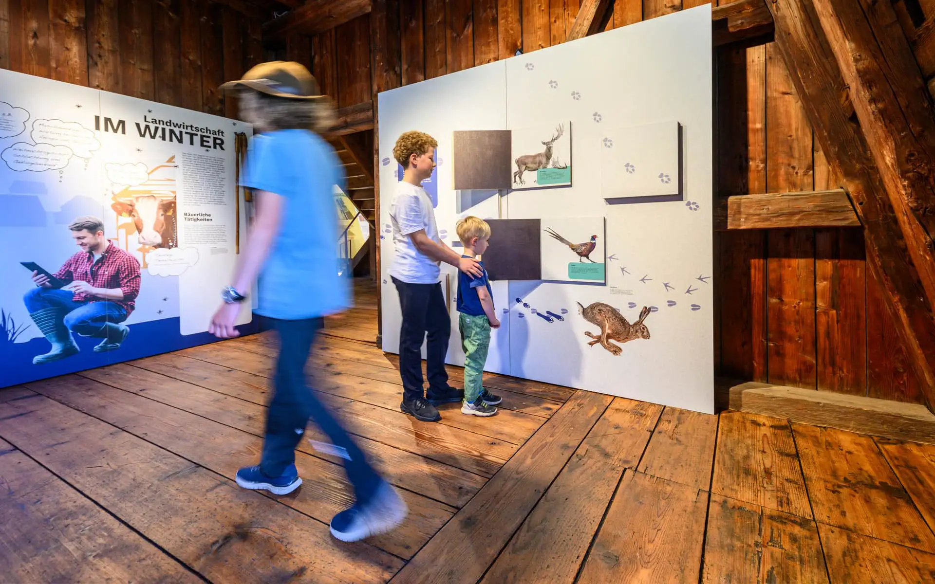 Kinder betrachten eine interaktive Station mit Tierspuren in einem hölzernen Ausstellungsraum.