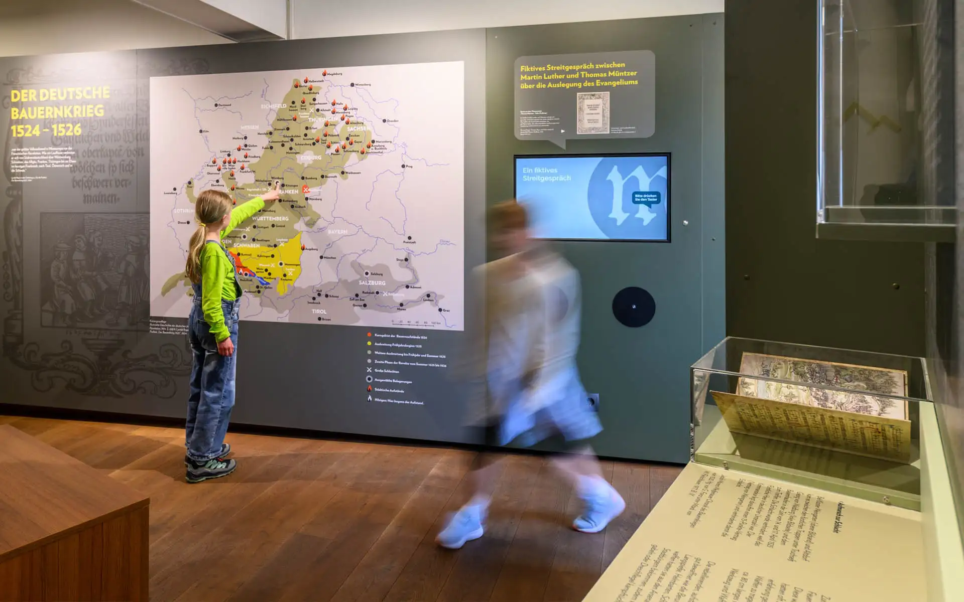 Kind zeigt auf eine große Karte zum Deutschen Bauernkrieg in einem Ausstellungsraum.