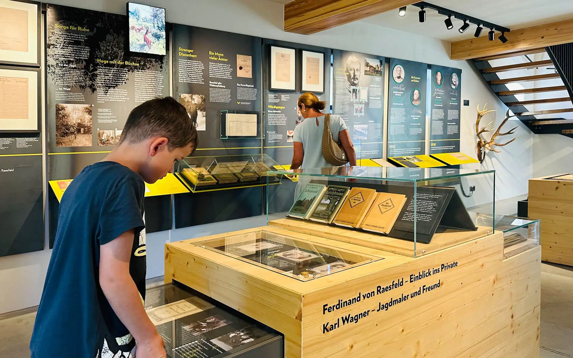 Junge und Besucherin betrachten Vitrinen und Informationstafeln in einem Museumsraum.