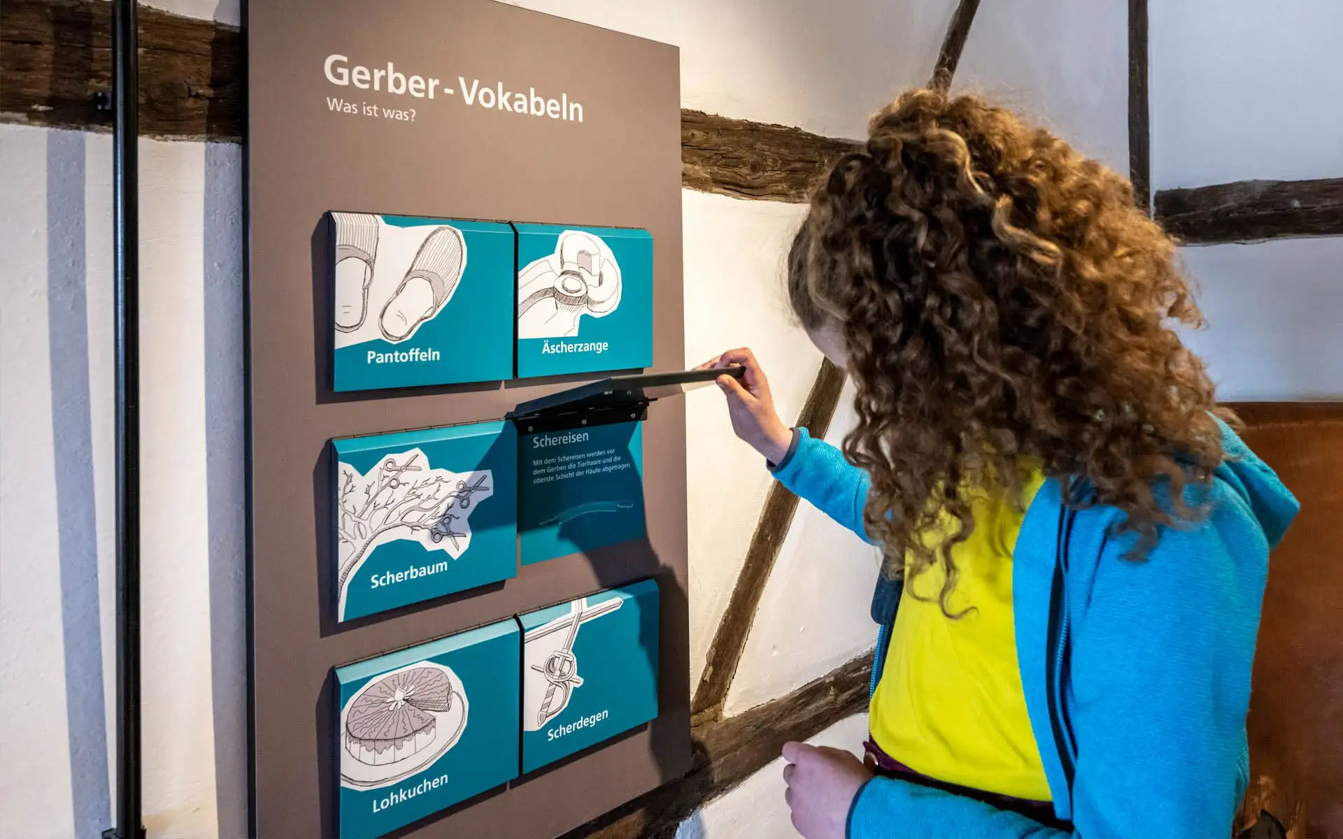 Kind öffnet an einer interaktiven Museumsstation zu Gerber-Vokabeln eine Klappe.