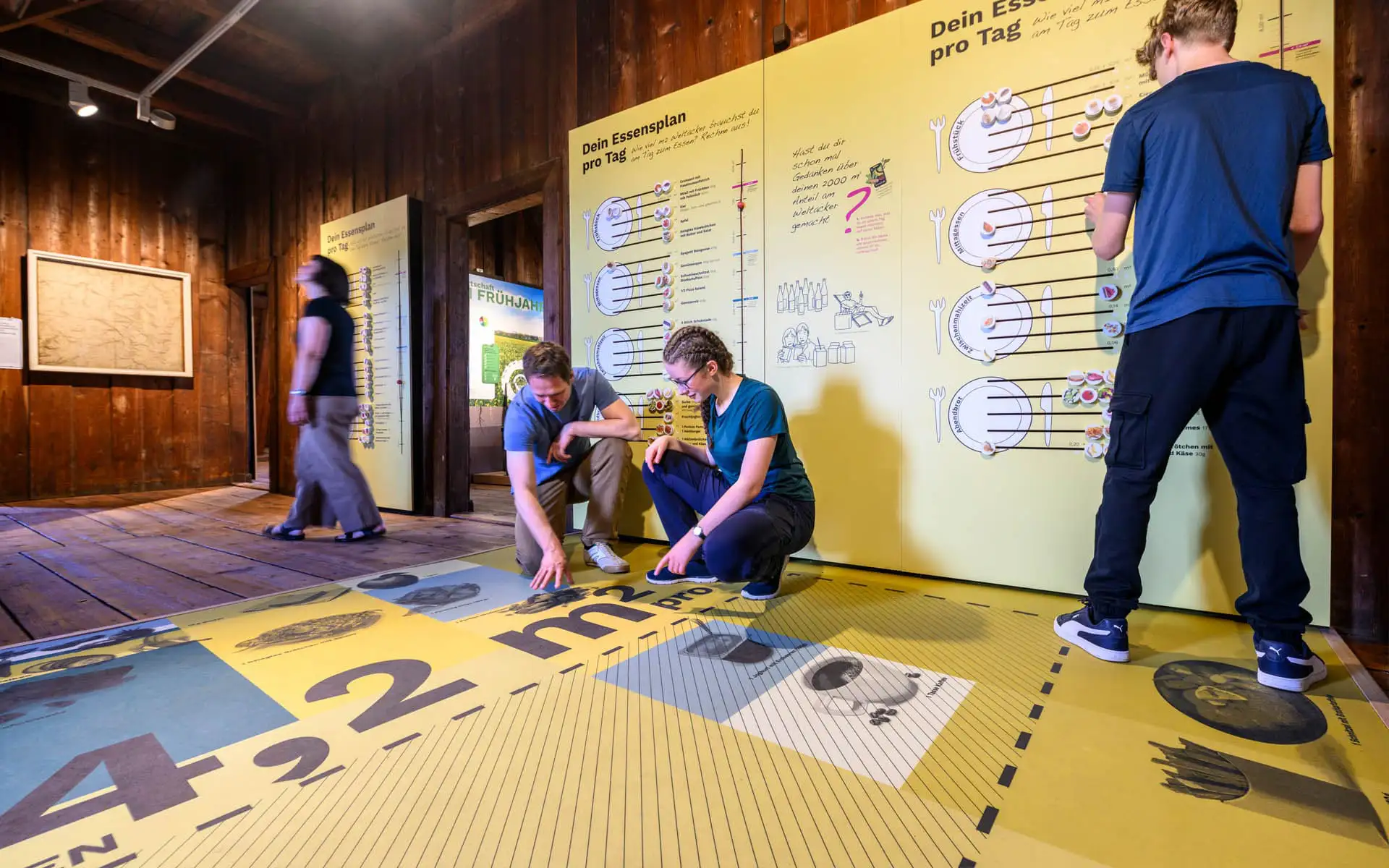 Besuchende nutzen in einem hölzernen Ausstellungsraum eine interaktive Station zum täglichen Essen.