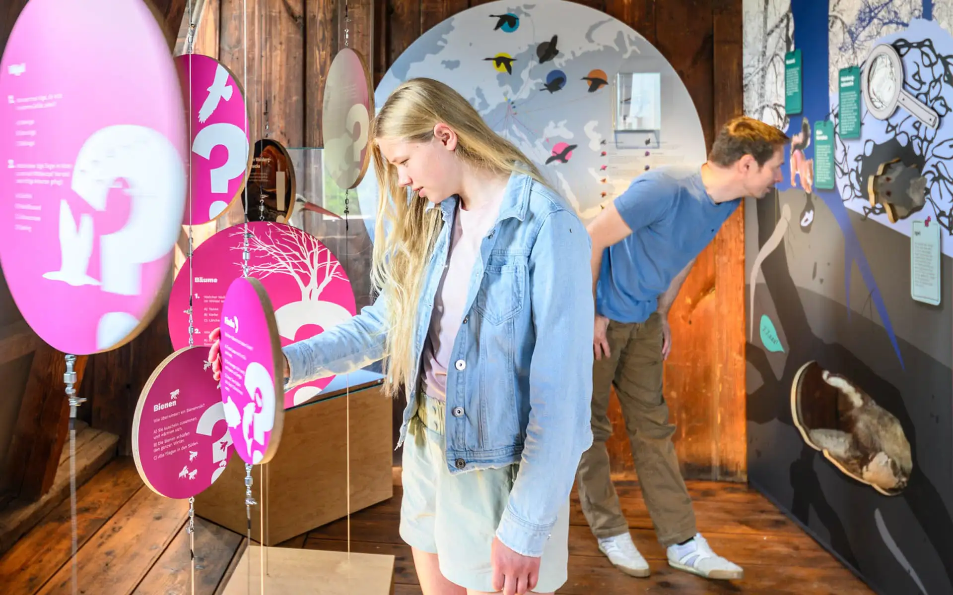 Jugendliche erkunden eine interaktive Ausstellung mit hängenden runden Informationselementen.