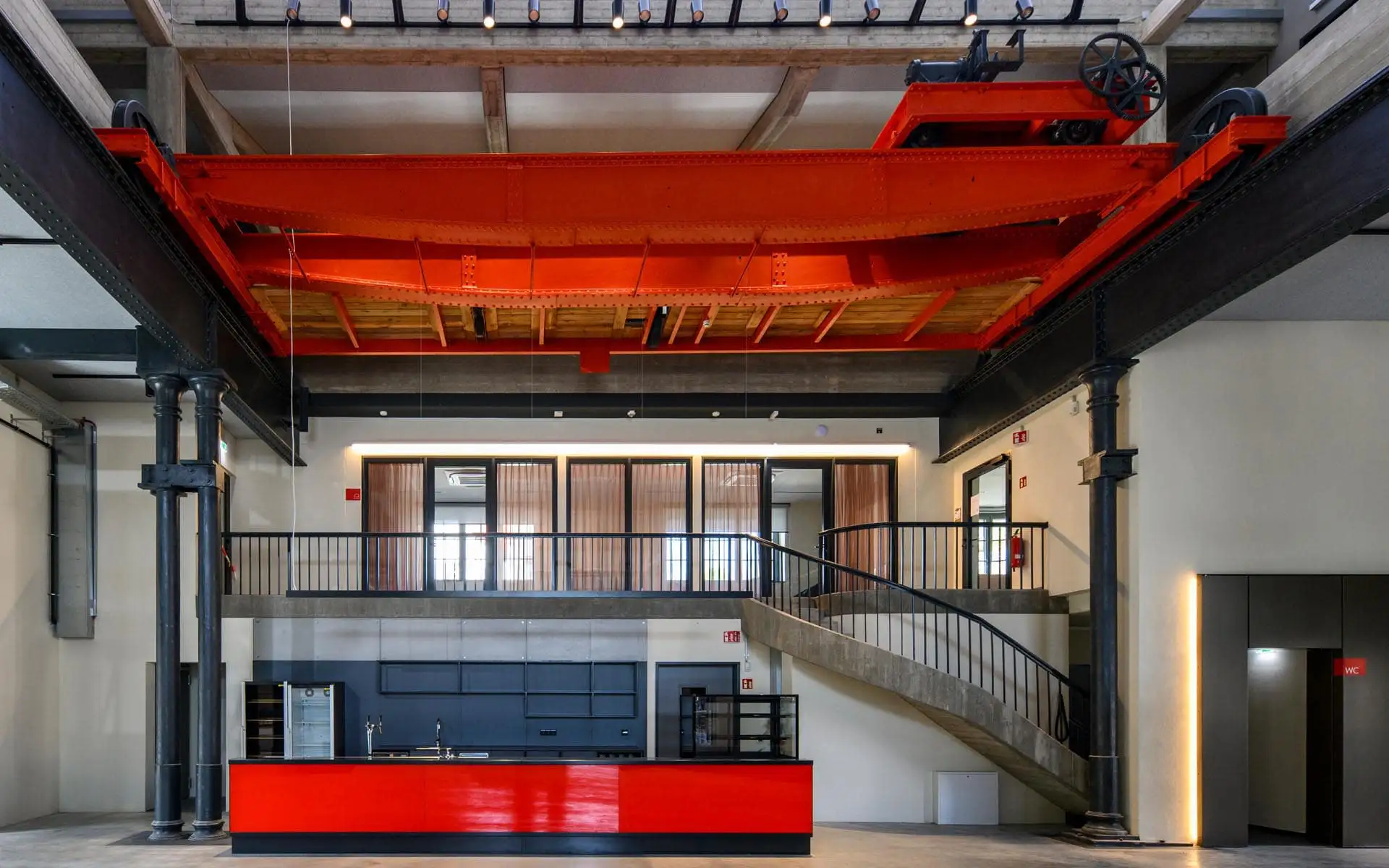 Industriehalle mit leuchtend roter Kranbahn, Bar und Galerieebene