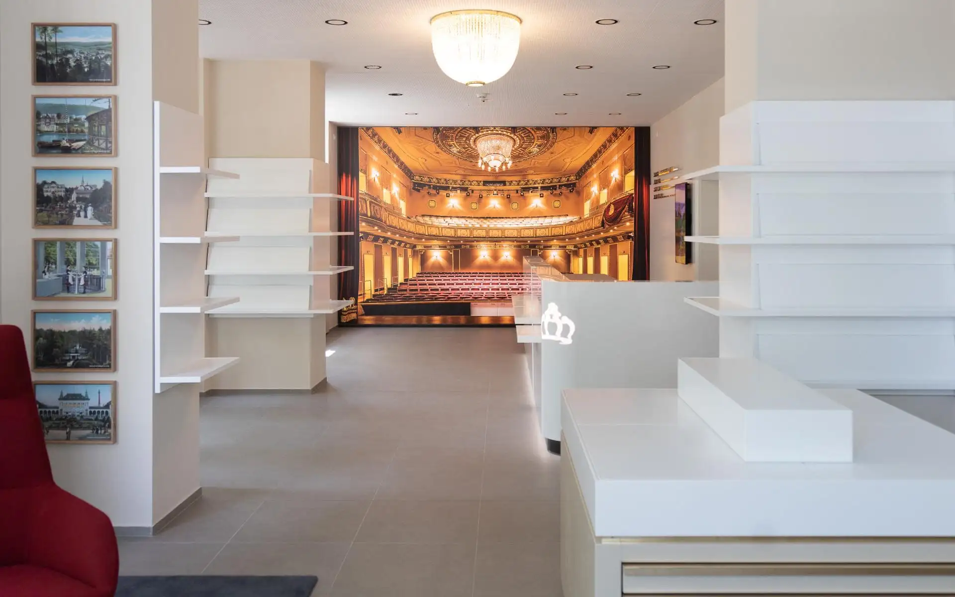 Blick durch die Tourist-Information auf weißen Tresen, Regale und das große Theater-Wandbild am Raumende.