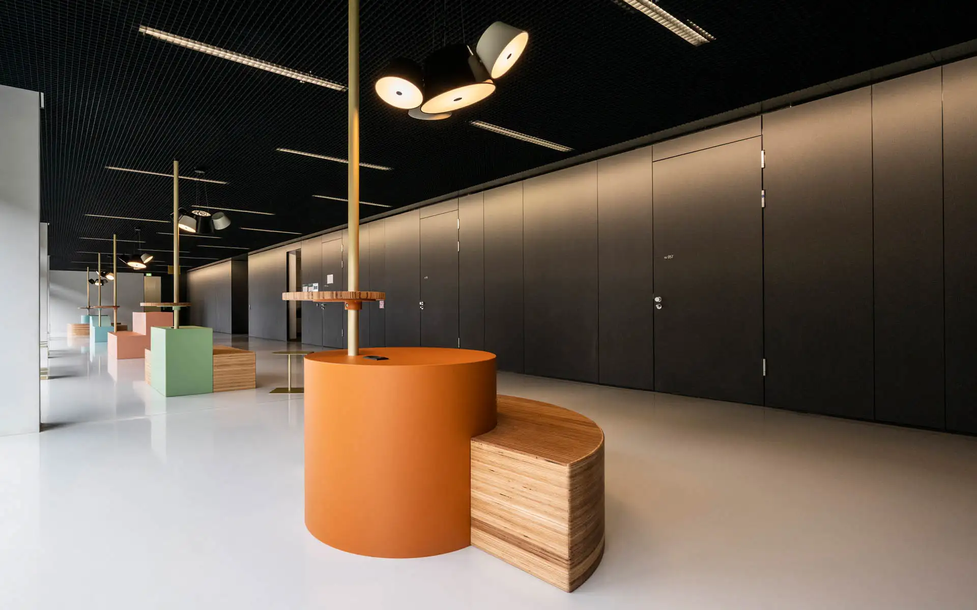 Langer Flur mit Sitzinseln: runder orangefarbener Tischkörper mit Holzbank, schwarze Decke mit Leuchten