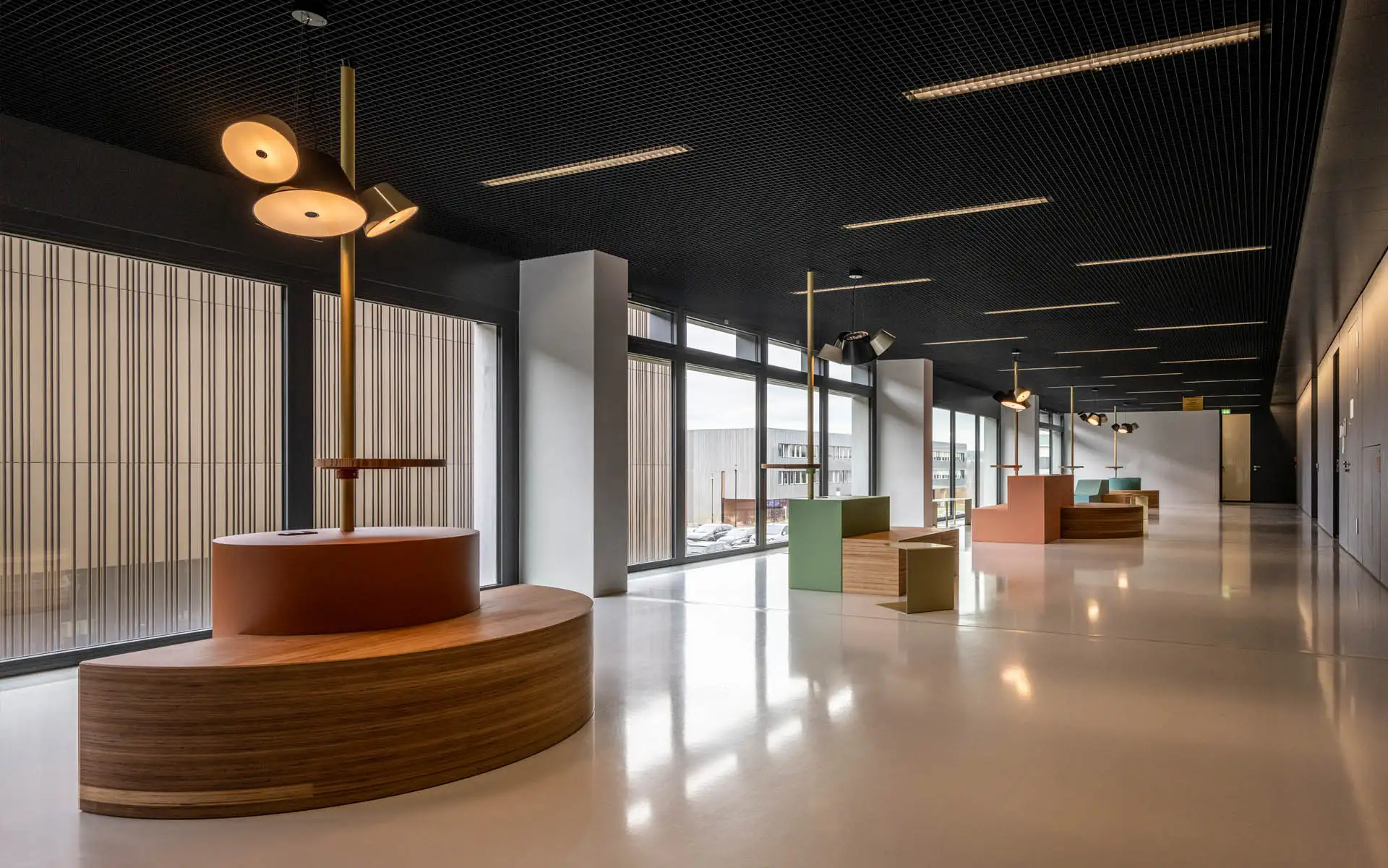 Flurbereich mit großen Fensterflächen und mehreren Sitzinseln aus Holz und farbigen Elementen