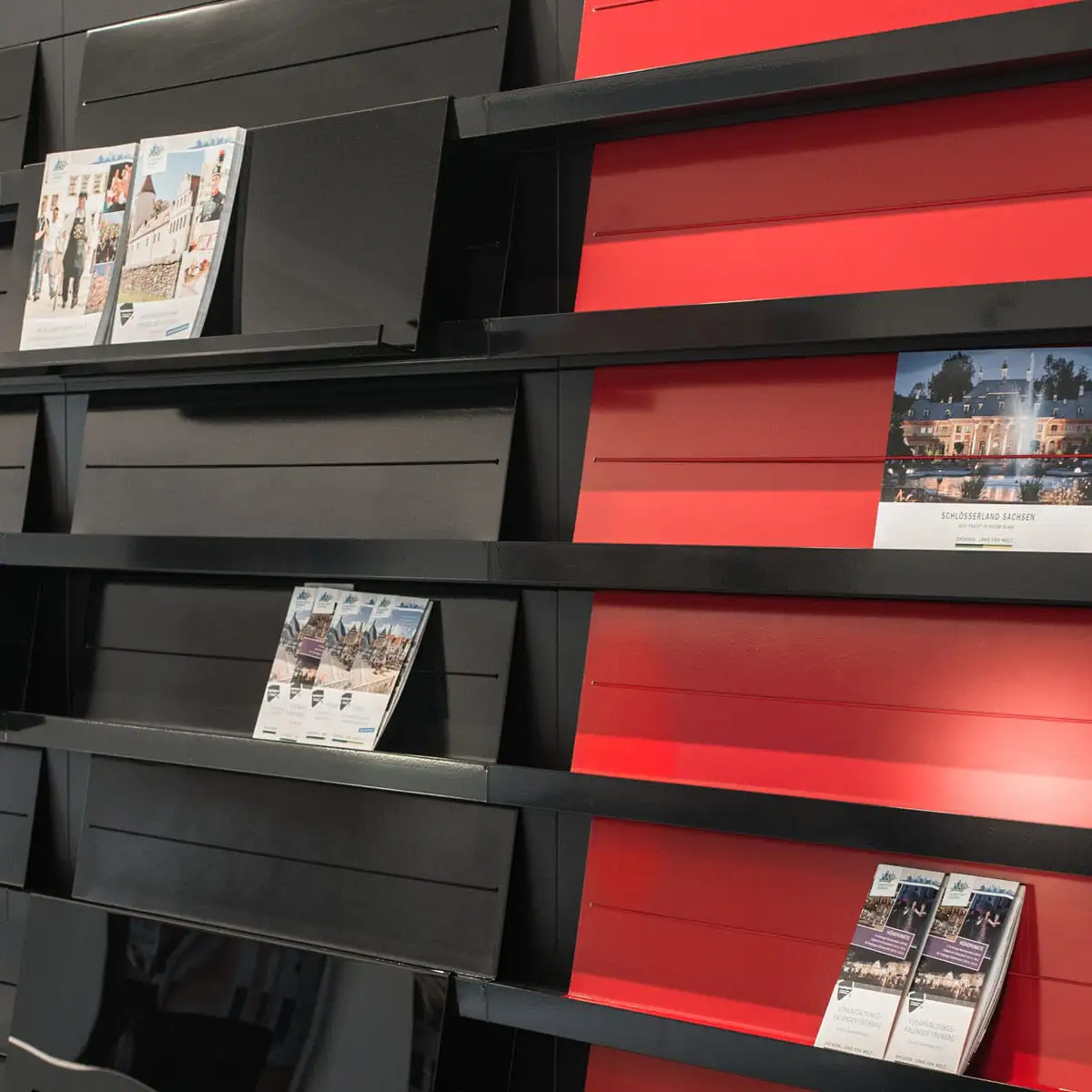Detail des modularen Wandregals mit schwarzen und roten Paneelen und ausgelegten Flyern