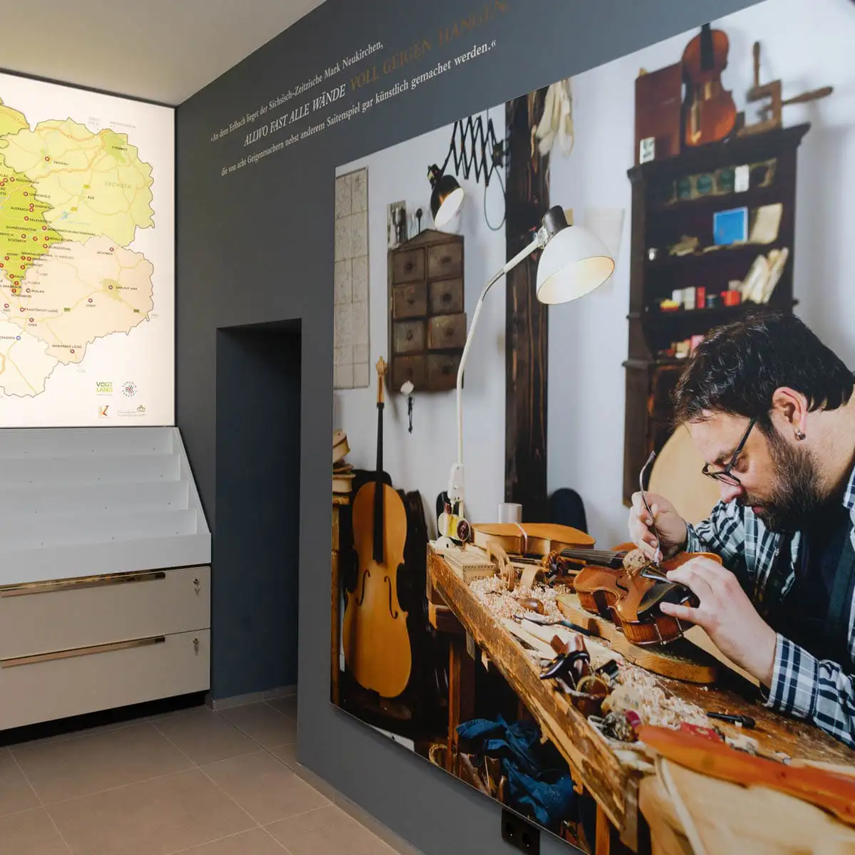 Infoecke mit großer Karte links und Wandfoto eines Geigenbauers an der Werkbank.