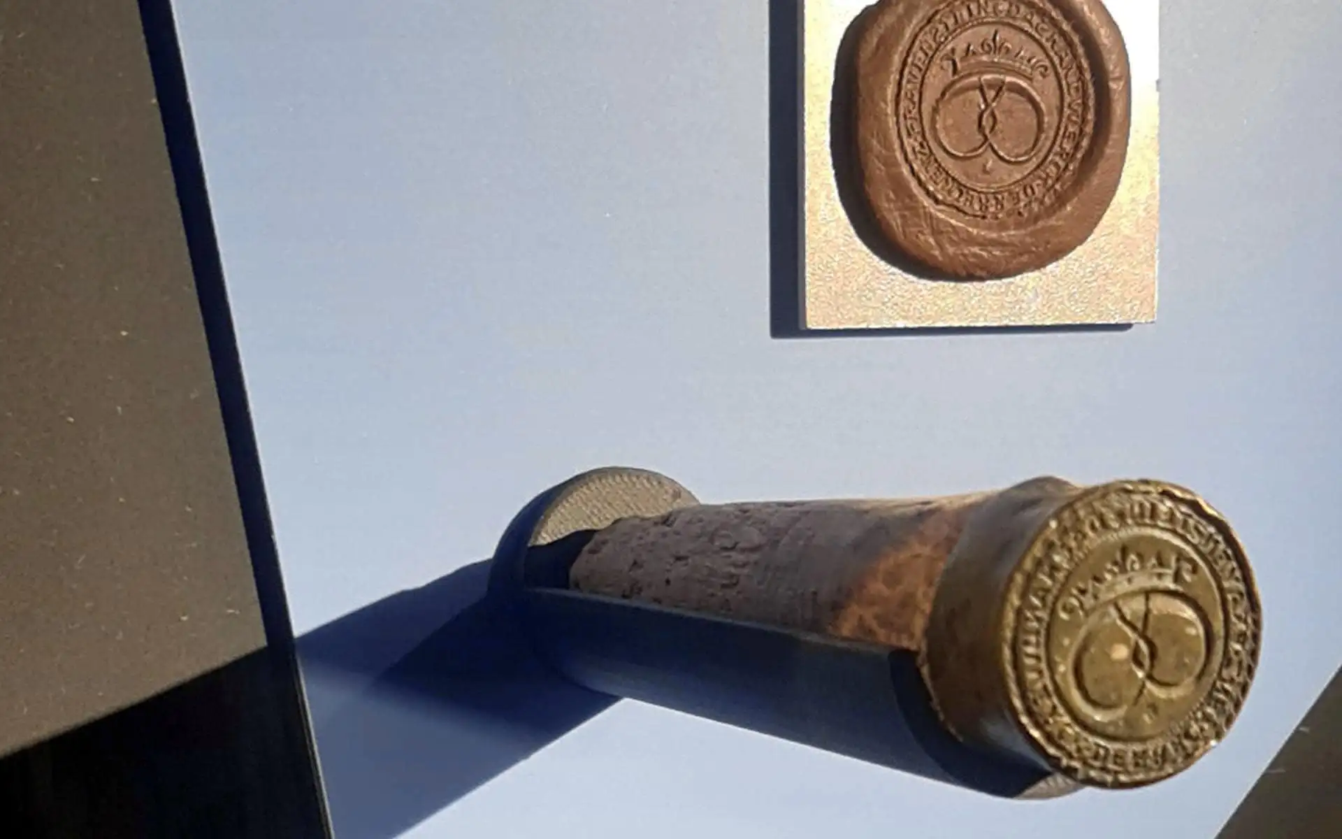 Historischer Siegelstempel mit geprägtem Emblem, präsentiert in einer flachen Vitrine.