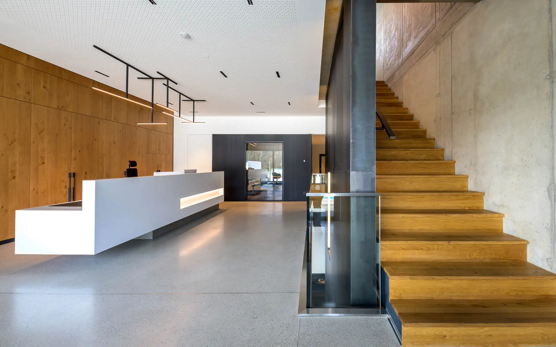 Moderner Empfangsbereich mit klarer Theke, Holzverkleidung, integrierter Beleuchtung und offener Treppenanlage.