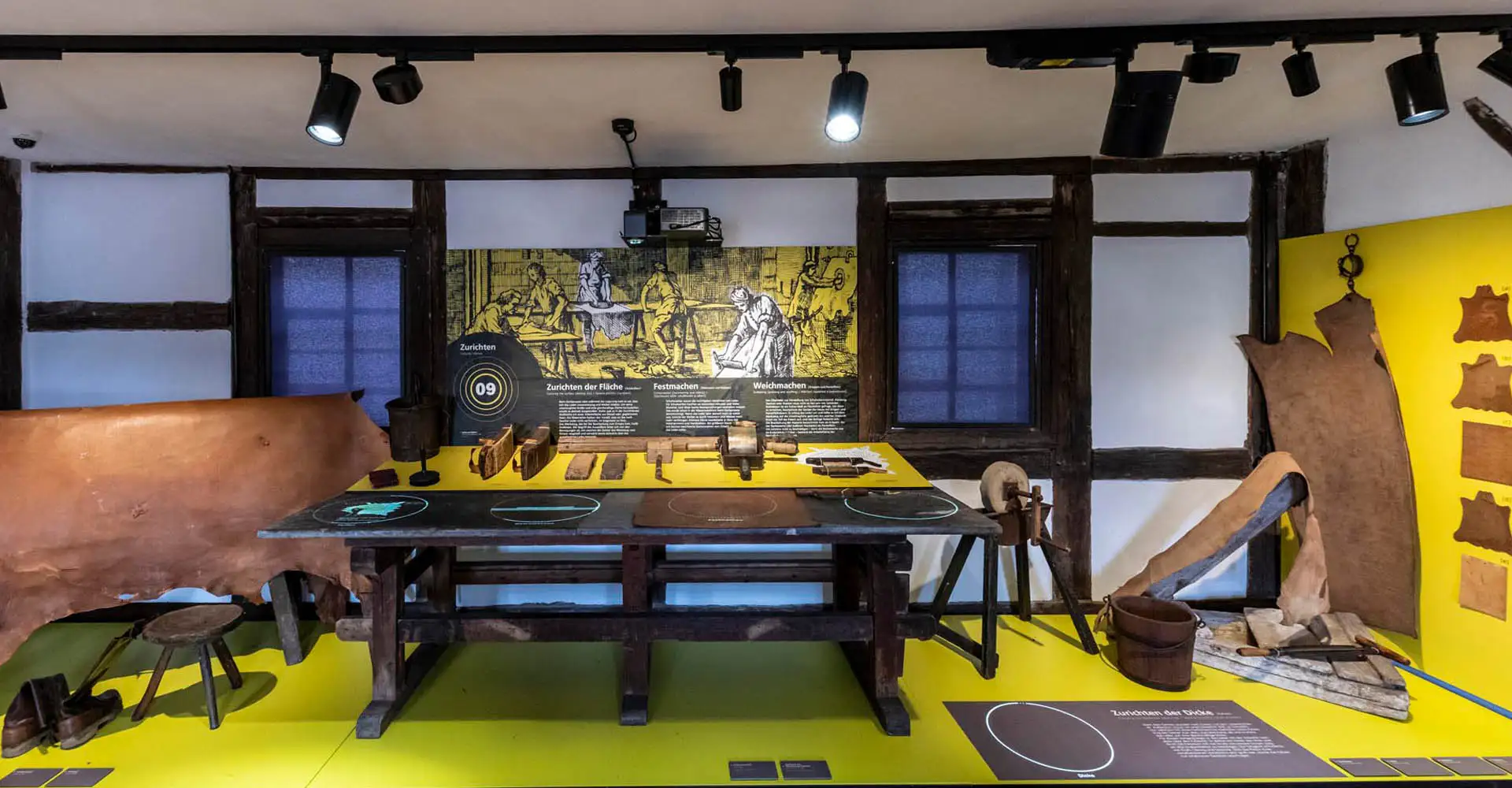 Ausstellungsraum mit gelbem Podest, Werkbank und Lederhandwerk-Exponaten im historischen Fachwerk.
