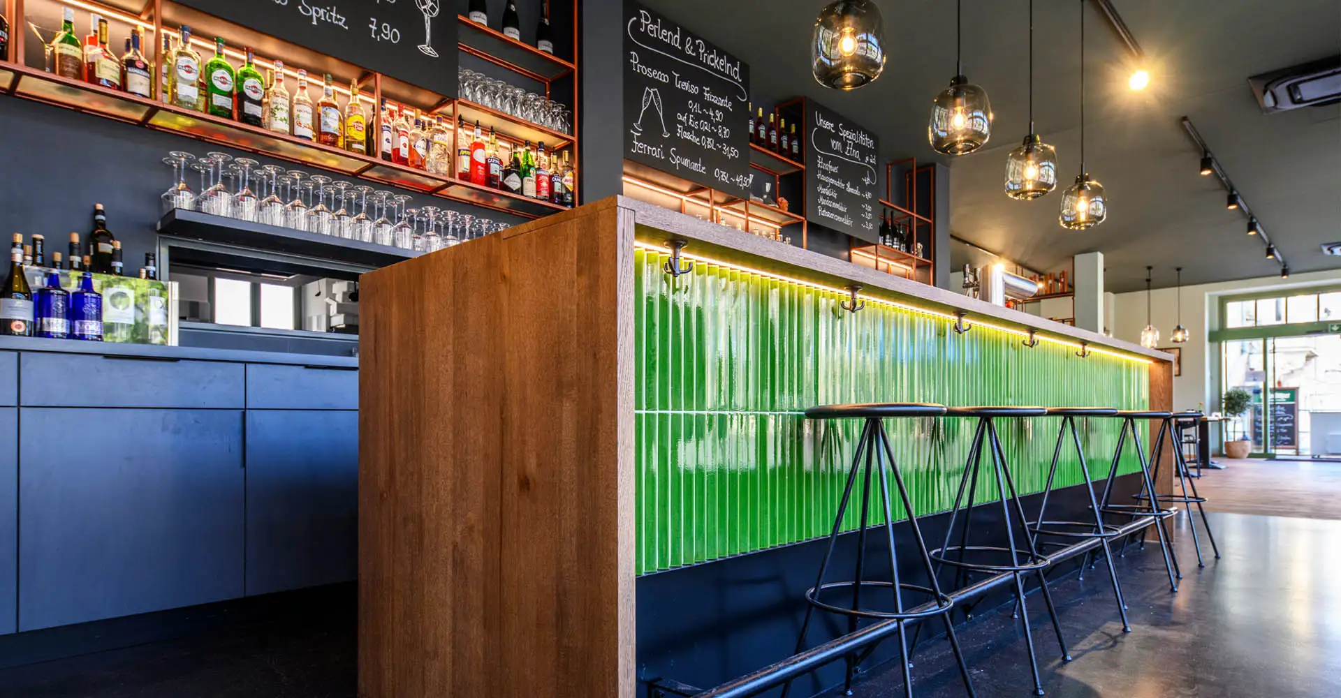 Modernes Restaurant mit langer grüner Bar, Hängelampen und gedeckten Tischen am Fenster.