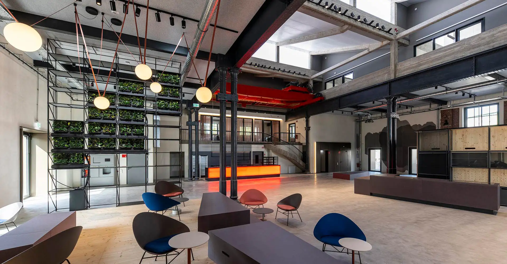 Großzügiges Foyer einer umgebauten Fabrik mit Sitzinseln, Pflanzenwand und Pendelleuchten.