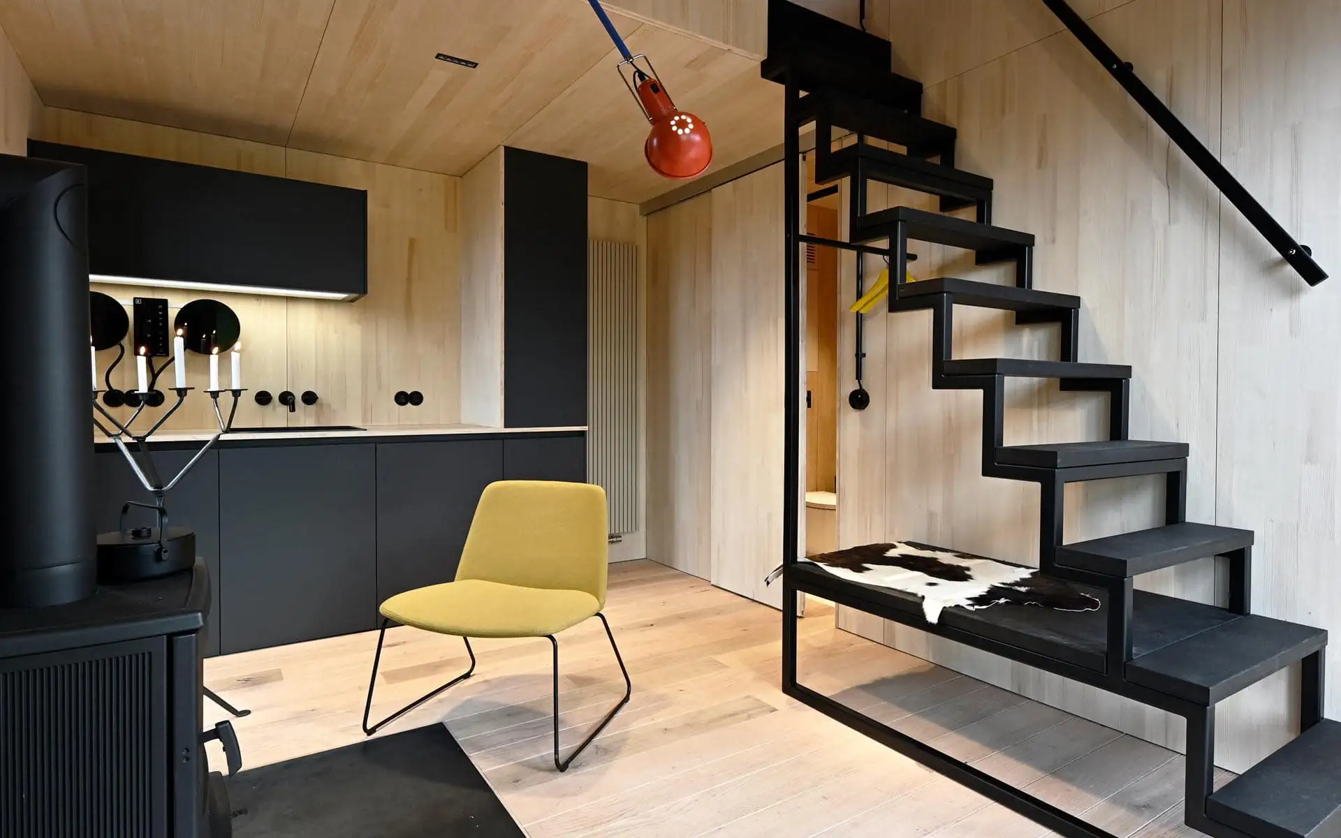 Moderne Küche mit schwarzen Fronten, gelbem Stuhl und offener Treppe aus Metall.