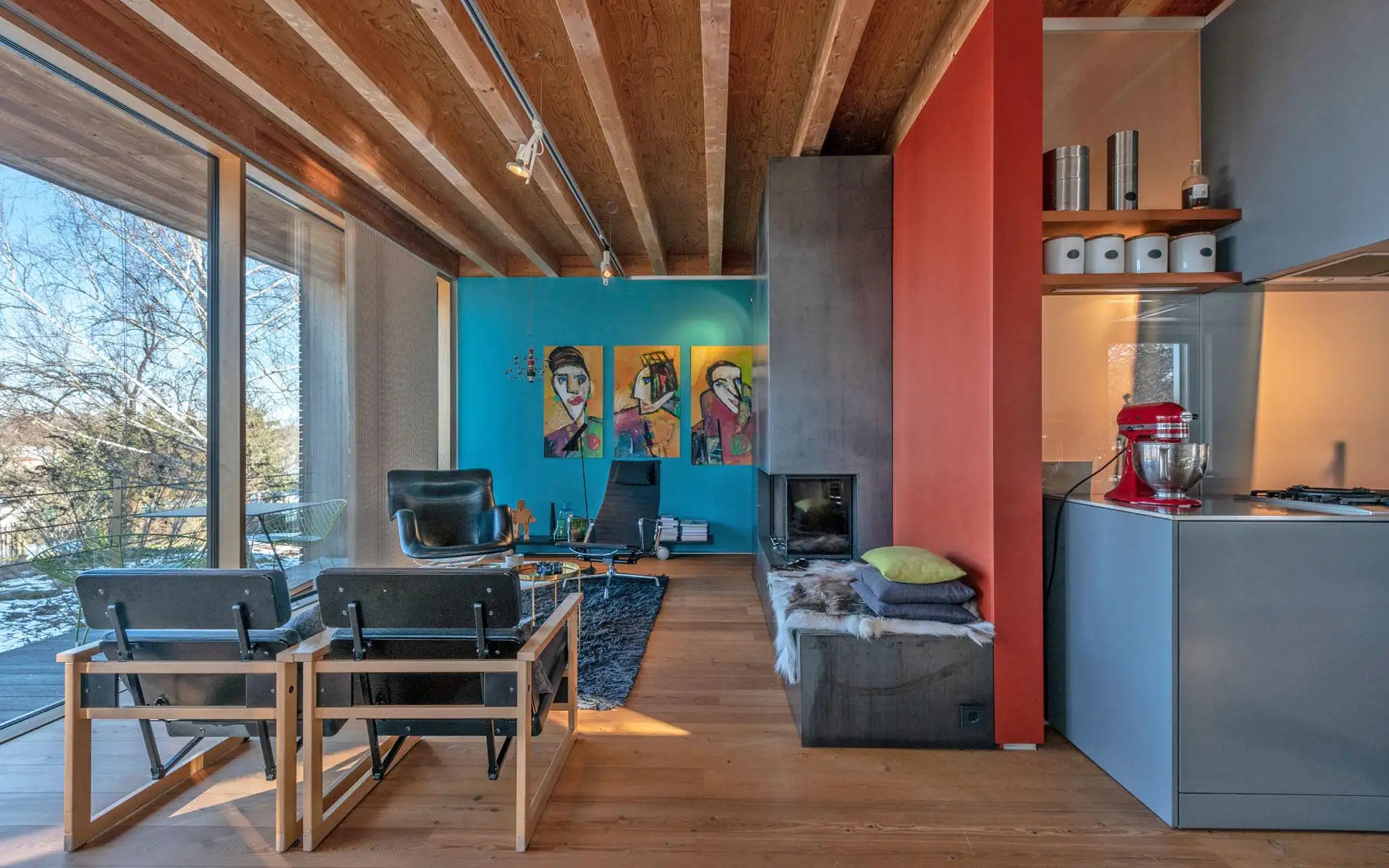 Offener Wohnraum mit Holzdecke, Sitzgelegenheiten, Kamin, türkisfarbener Wandkunst und Küchenblock.