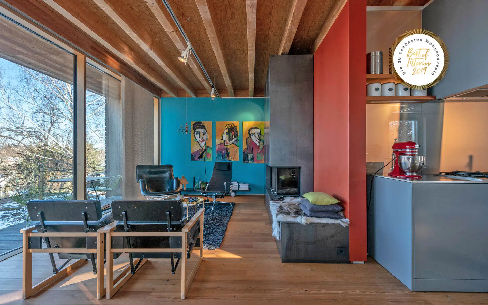Offener Wohnraum mit Holzdecke, Sitzgelegenheiten, Kamin, türkisfarbener Wandkunst und Küchenblock.