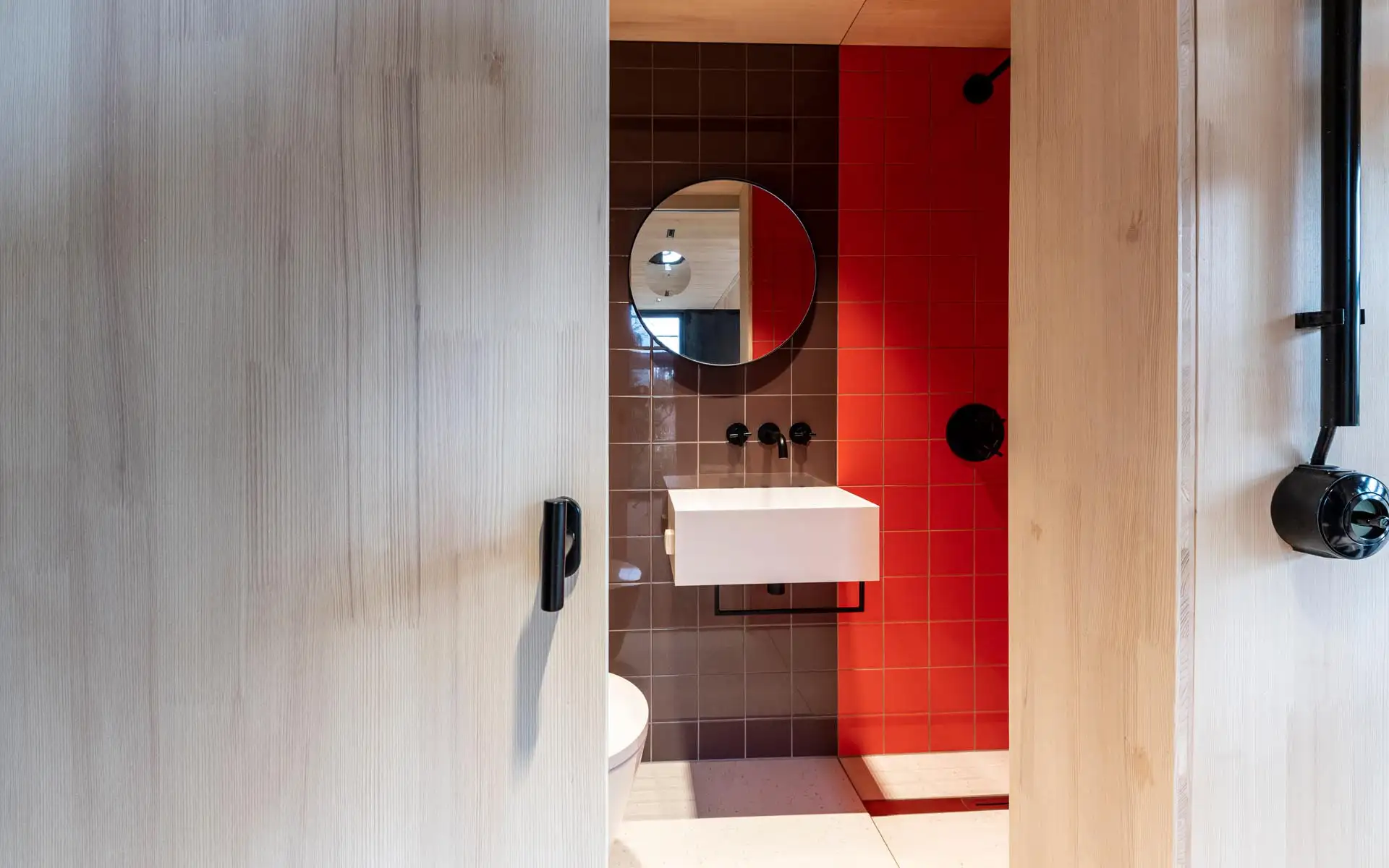 Badezimmer mit roten und braunen Fliesen, rundem Spiegel und weißem Waschtisch