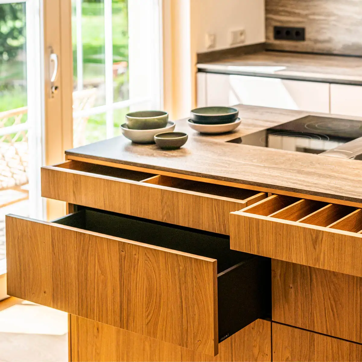Offene Schubladen einer Kücheninsel zeigen Holzfächer und hochwertiges Innenleben.
