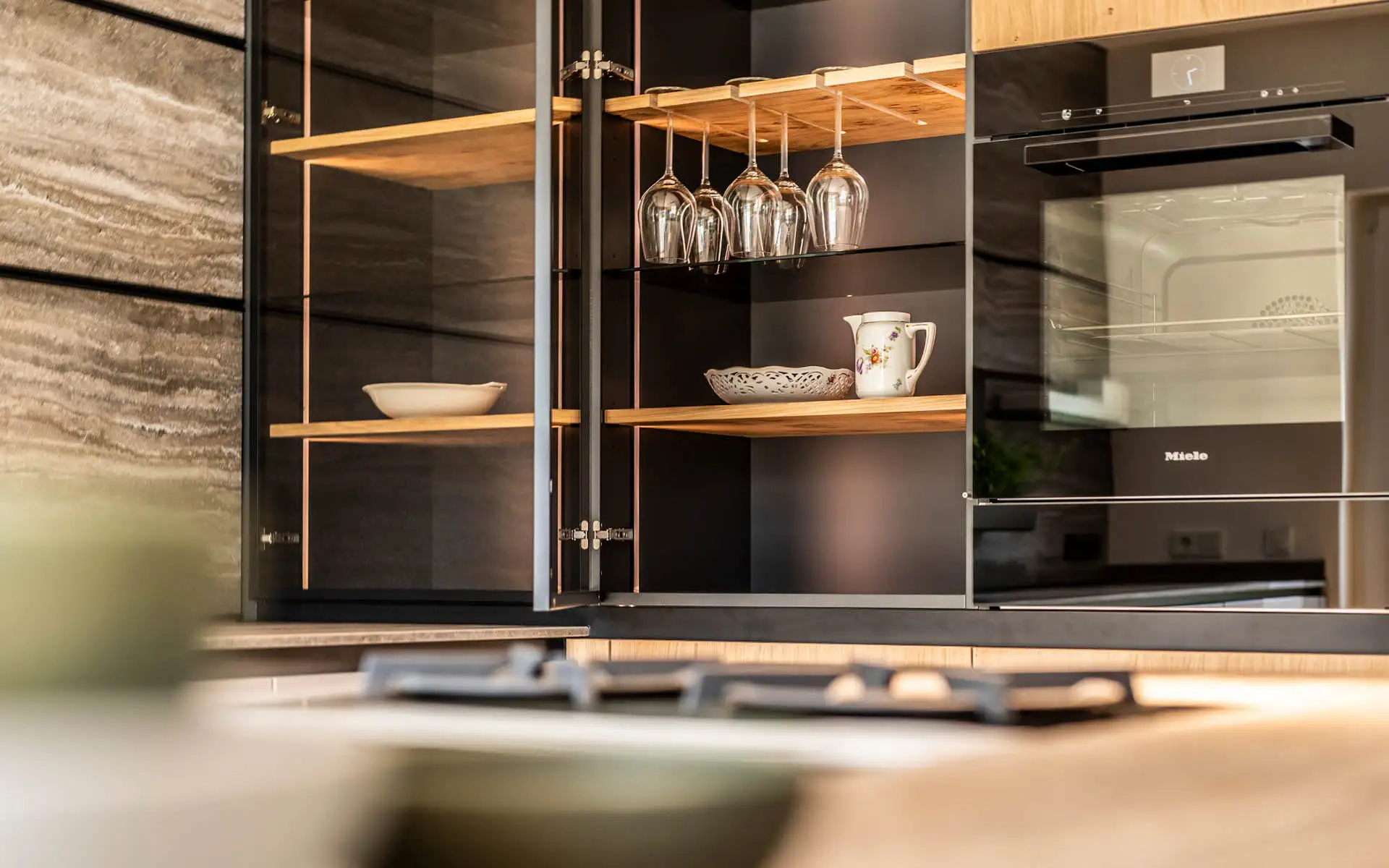 Detail eines geöffneten Glashängeschranks mit Gläsern und Geschirr.